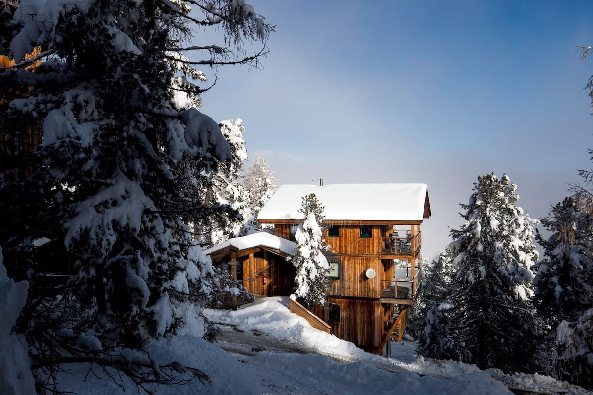 A wooden cabin with a balcony, surrounded by snow-covered trees.