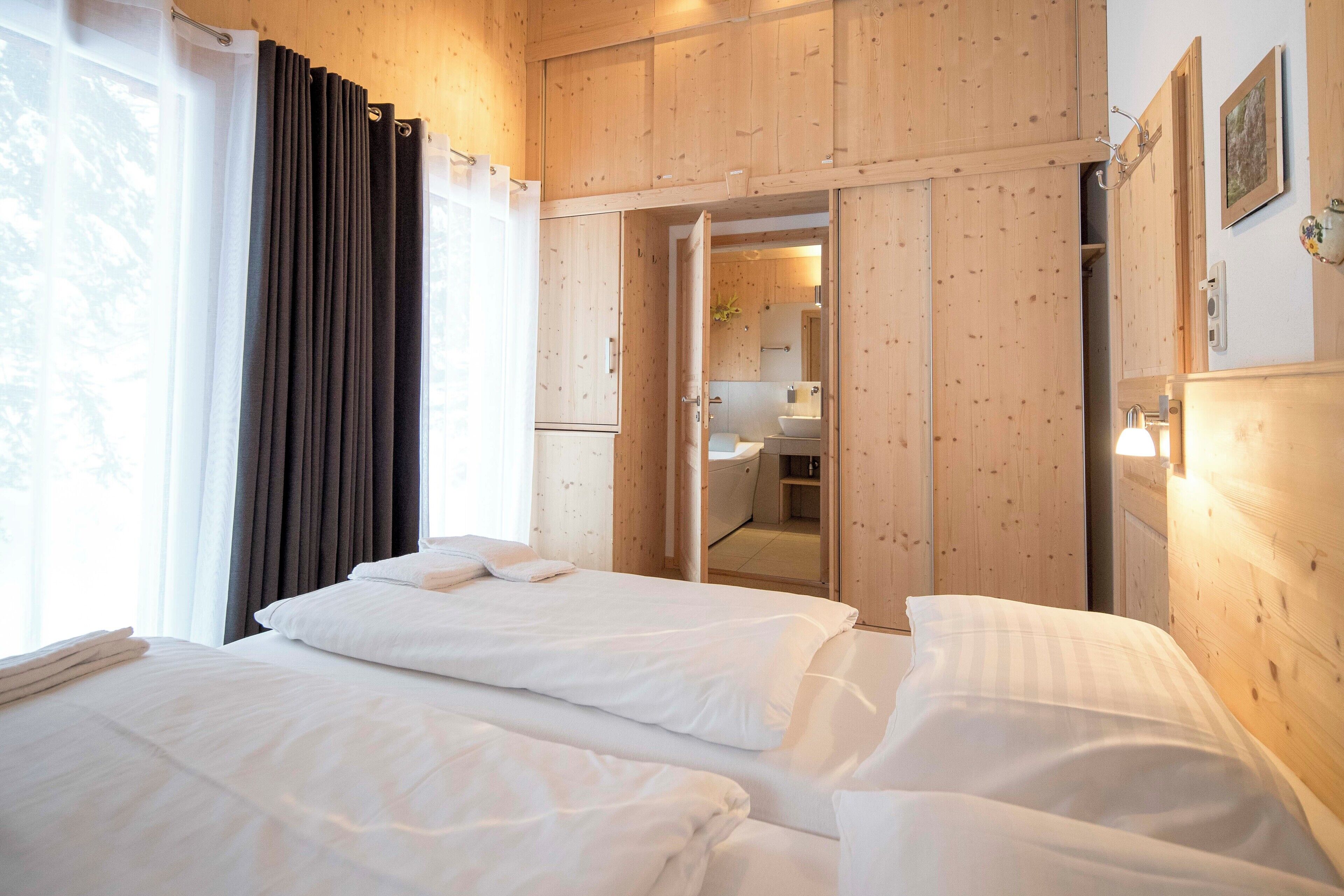 Een hotelkamer met twee bedden, een badkamer zichtbaar door een open deur, houten wanden en een raam met gordijnen.