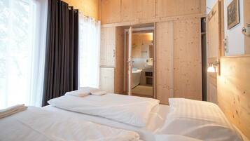 Een hotelkamer met twee bedden, een badkamer zichtbaar door een open deur, houten wanden en een raam met gordijnen.