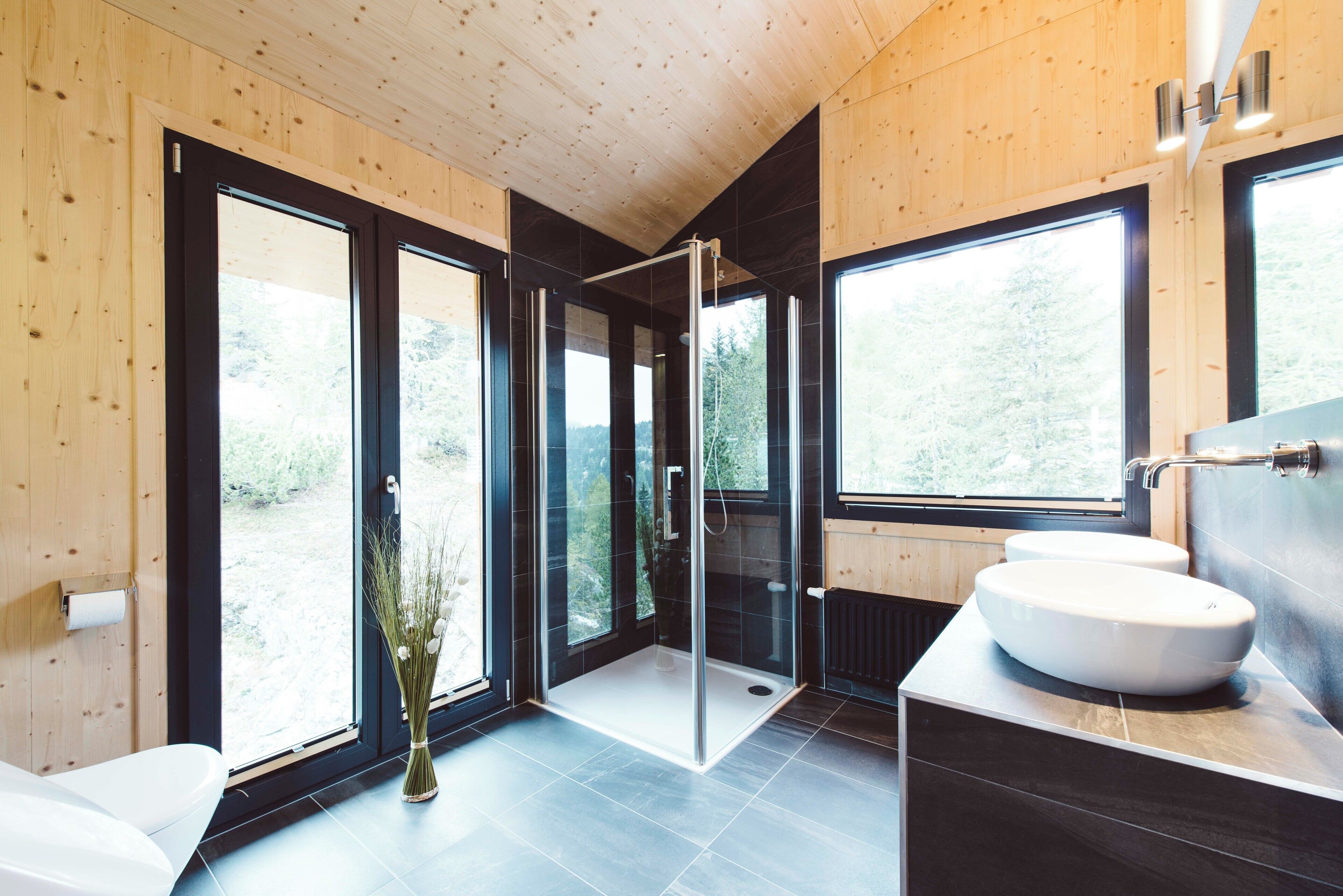 A modern bathroom with a glass shower enclosure, large windows, and a white sink.