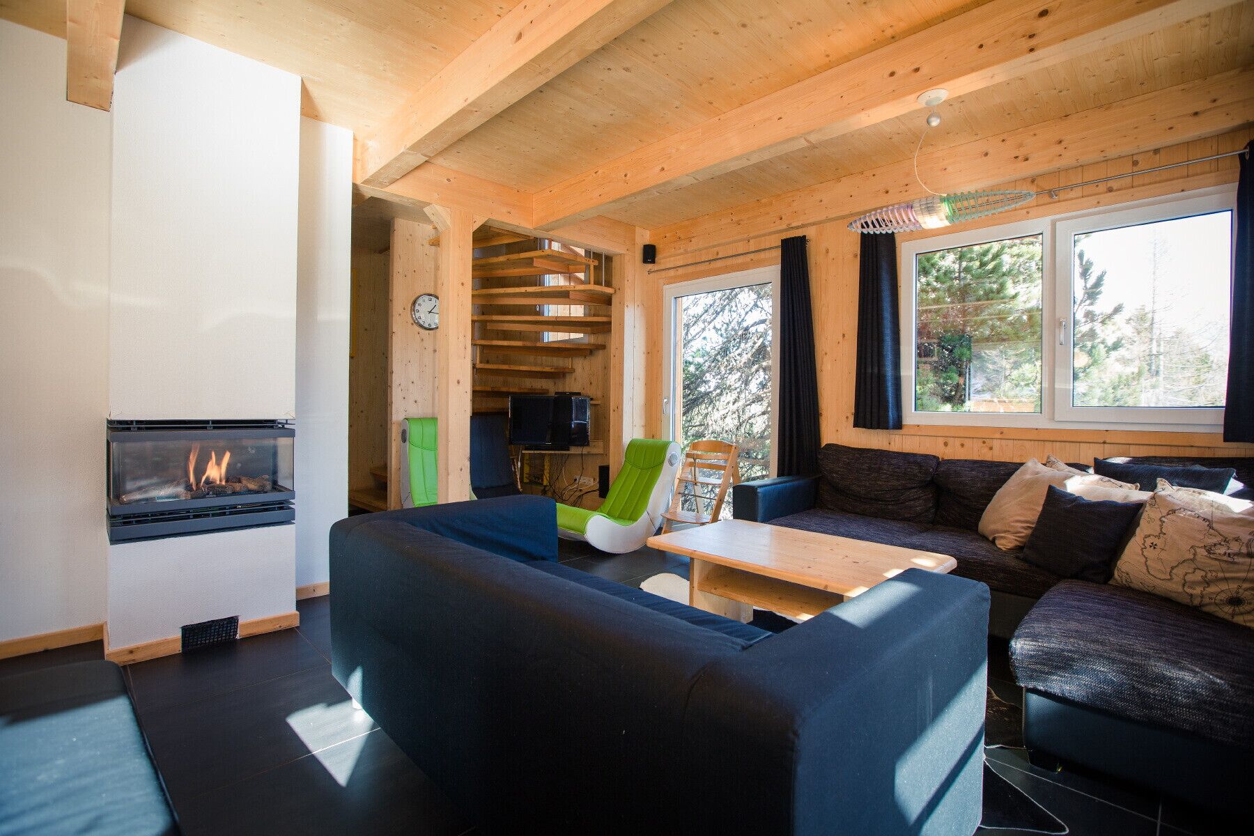 A cozy cabin interior with a fireplace, a sofa, a dining table, and a large window offering a view of trees.