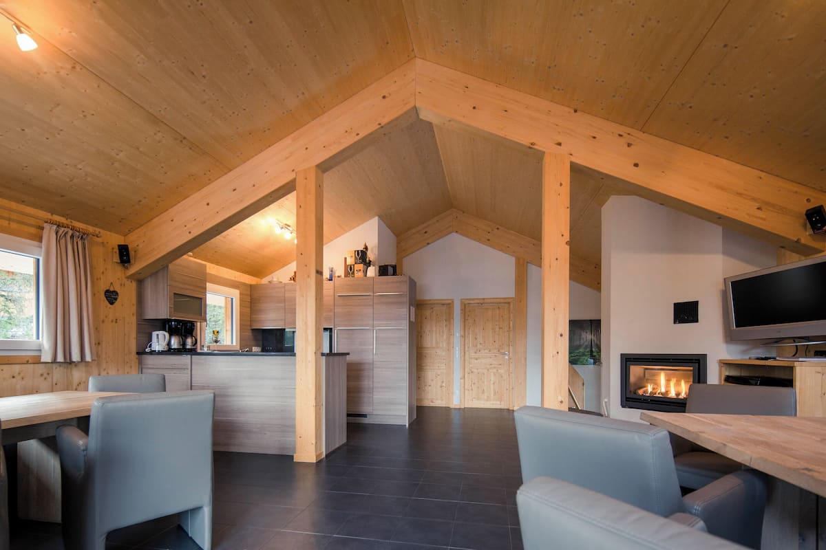 A spacious cabin with a high ceiling, a fireplace, a television, and a dining area with chairs.