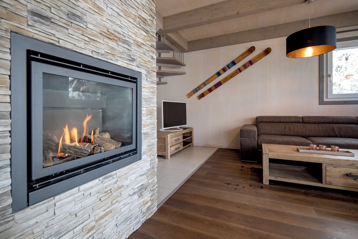 A modern living room with a stone accent wall, a fireplace, a wooden coffee table, and a large window.