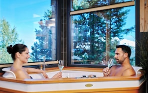 A couple in a hot tub with a view of trees and a building outside. - Alpenpark Turracher Höhe by ALPS RESORTS (Turracher Höhe)