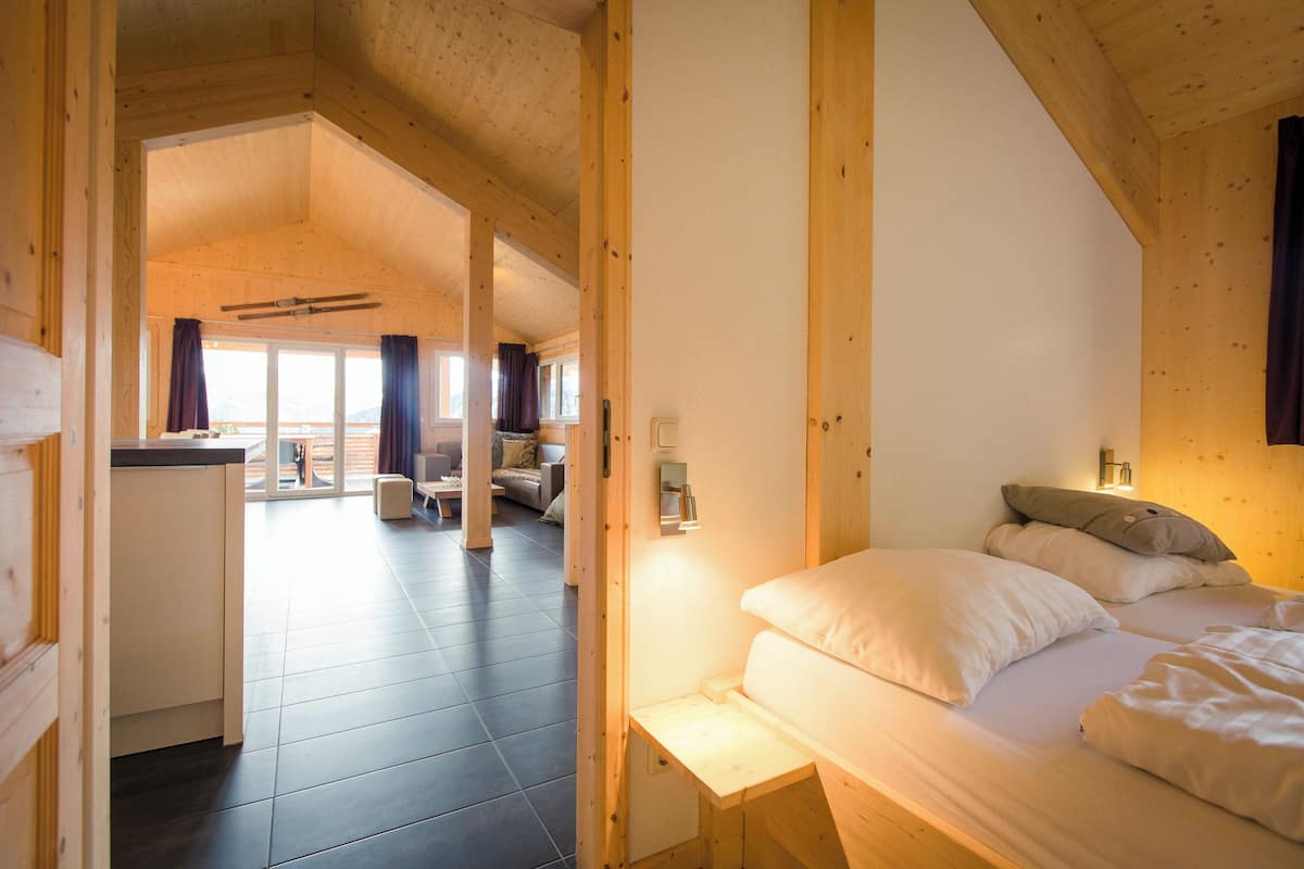 A wooden interior with a bed, a small desk, and a view of a balcony.