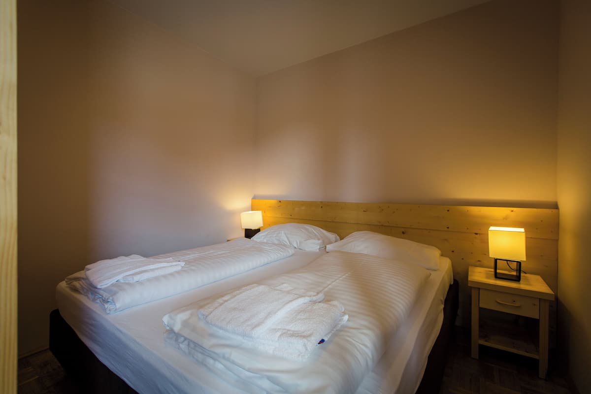 A double bed with white linens and two bedside tables with lamps.