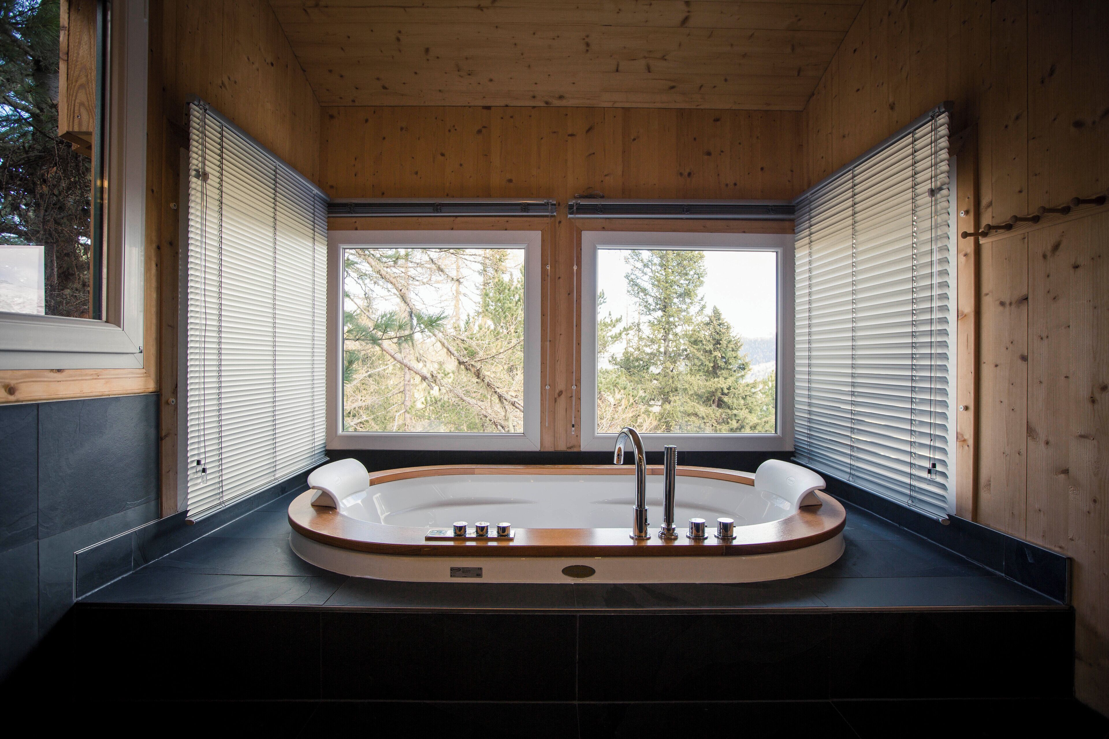 Un baño moderno con una bañera independiente, paredes de madera y ventanas amplias con vistas a árboles.