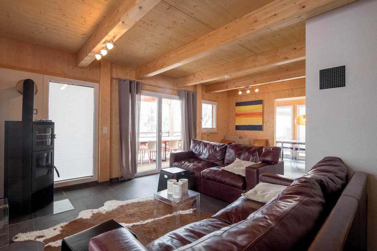 A spacious living room with a large brown leather sofa, a glass coffee table, and a wooden ceiling.