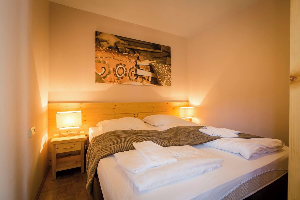 A neatly made bed with folded towels, a wooden headboard, and two bedside lamps.