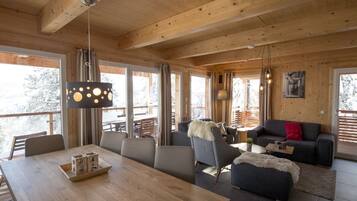 A spacious living area with a wooden ceiling, large windows, and a cozy seating arrangement.