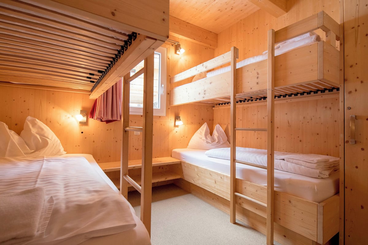 A wooden cabin room with bunk beds, a window, and a wall-mounted light fixture.