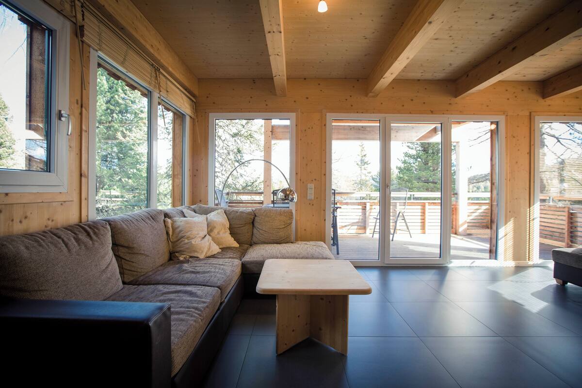 A modern living room with a sectional sofa, a wooden coffee table, and large windows offering a view of the outdoors.