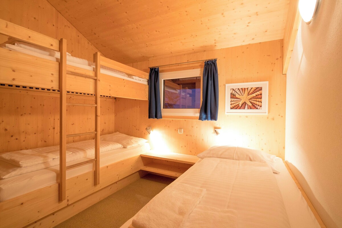A bunk bed room with a ladder, a small window with curtains, and a framed picture on the wall.