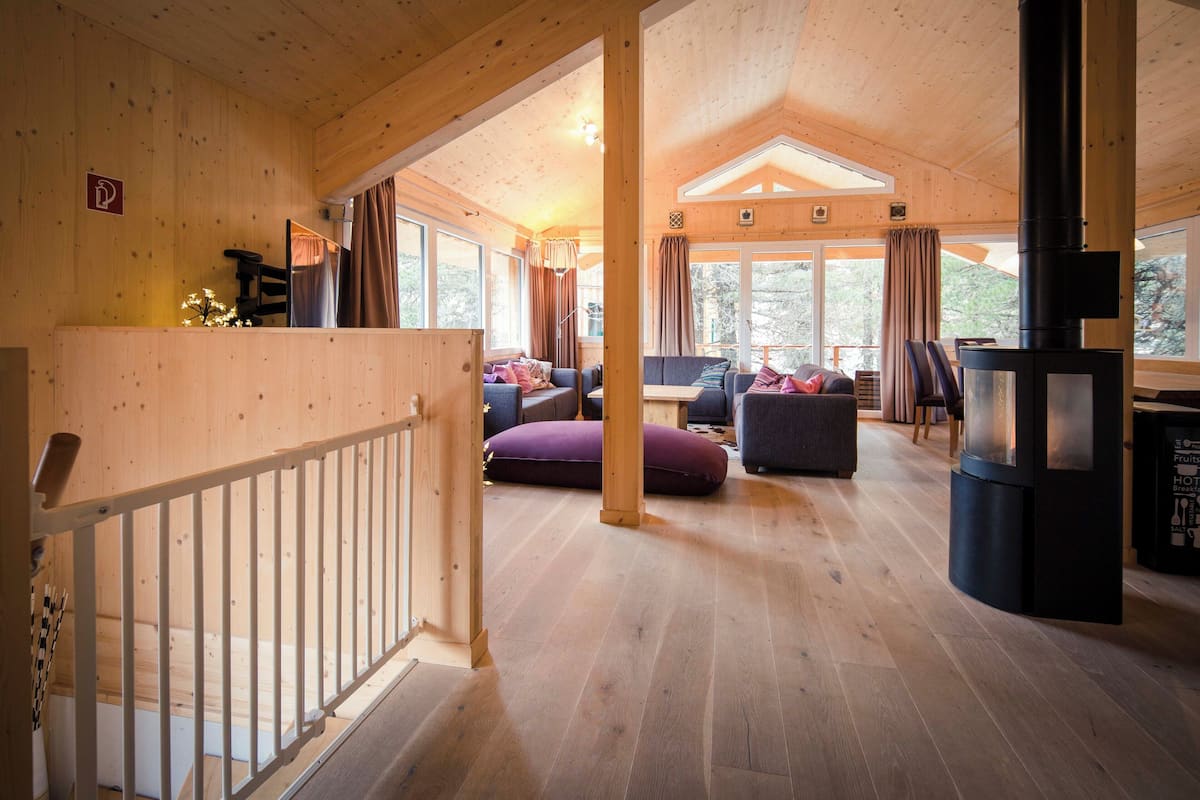 A wooden cabin interior with a living area, a fireplace, and large windows.