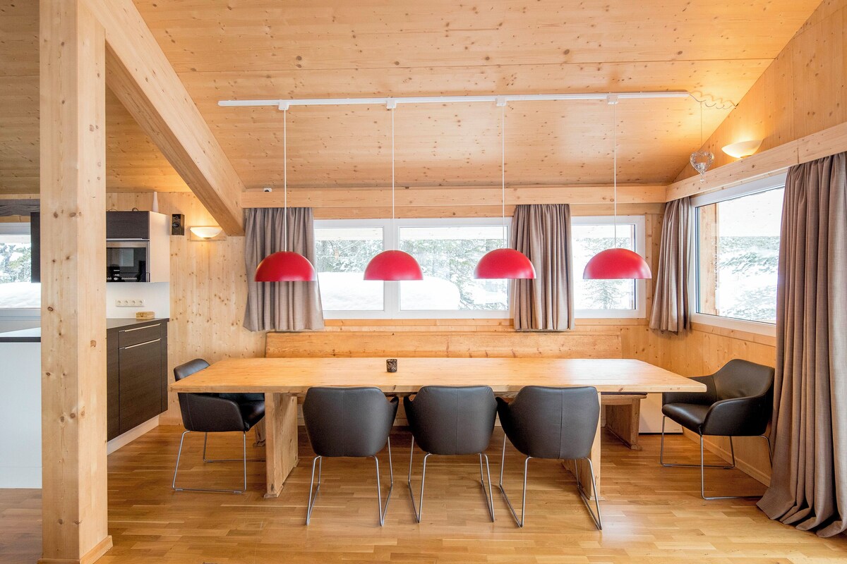 A wooden interior with a large dining table, four chairs, and three pendant lights.