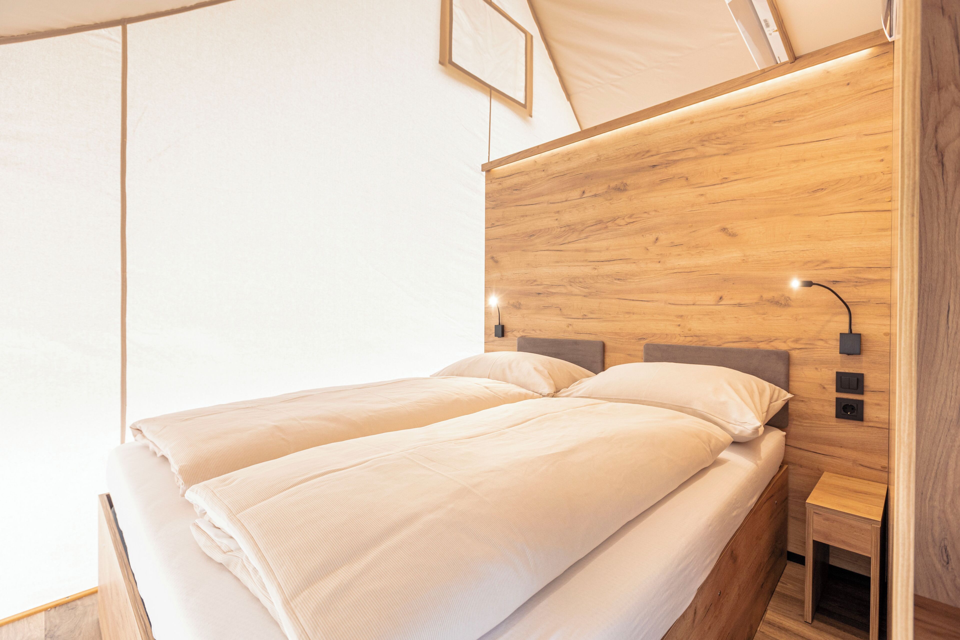 Een tweepersoonsbed met een houten hoofdbord, een nachtkastje en een wandlamp.
