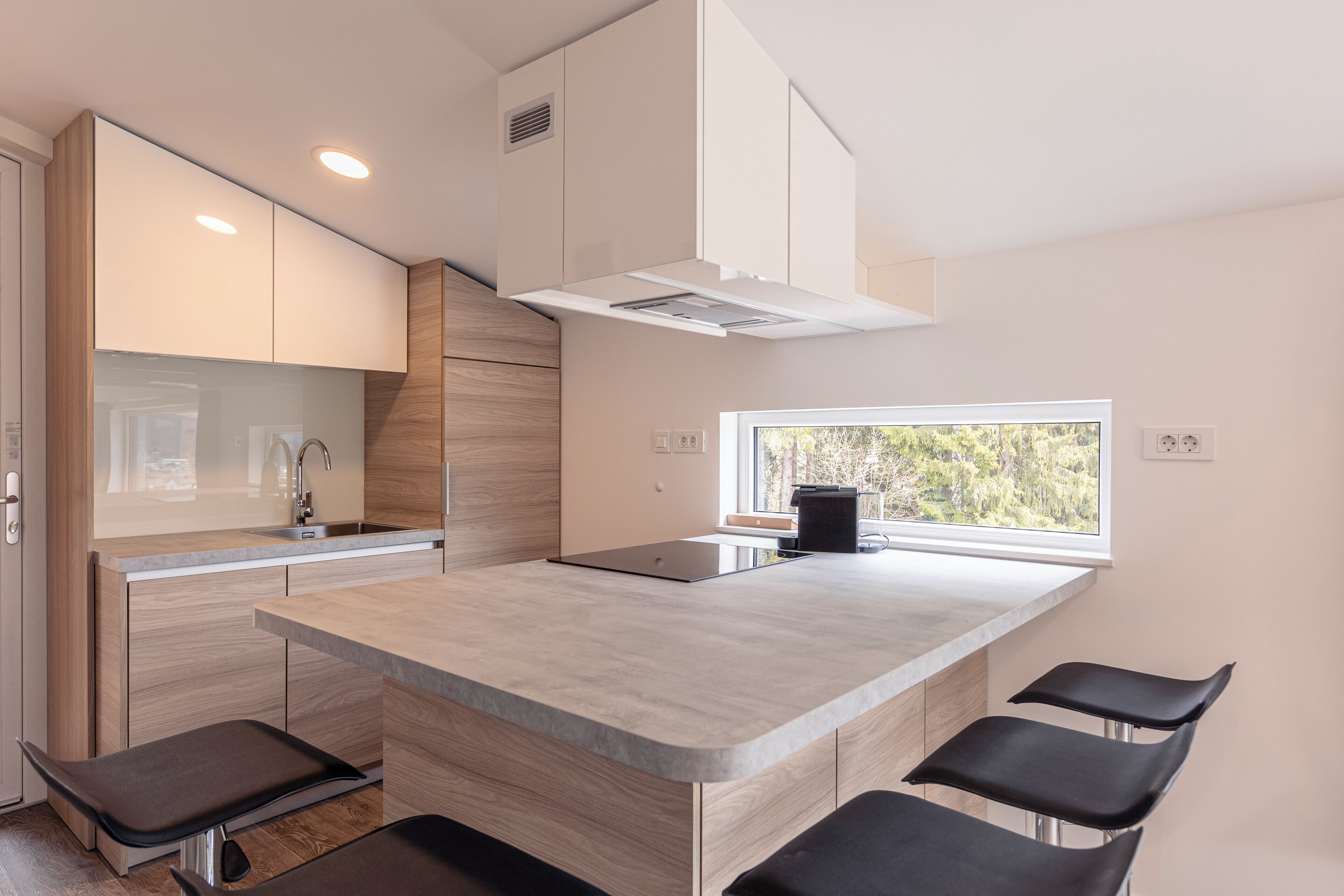 A modern kitchen with a central island, bar stools, and a window providing a view.