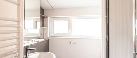 A bathroom with a white sink, a toilet, and a window above the toilet.