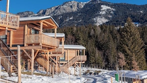 A wooden cabin with multiple balconies and a mountain backdrop. - Chalets & Glamping Nassfeld by ALPS RESORTS (Kotschach-Mauthen)
