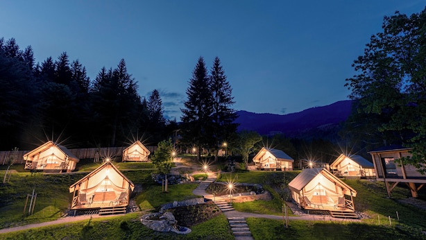 A row of wooden cabins with a pathway leading to each, surrounded by greenery and trees. - Chalets & Glamping Nassfeld by ALPS RESORTS (Kotschach-Mauthen)