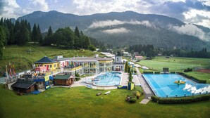 A hotel with a swimming pool, outdoor seating, and a view of mountains. - Chalets & Glamping Nassfeld by ALPS RESORTS (Kotschach-Mauthen)
