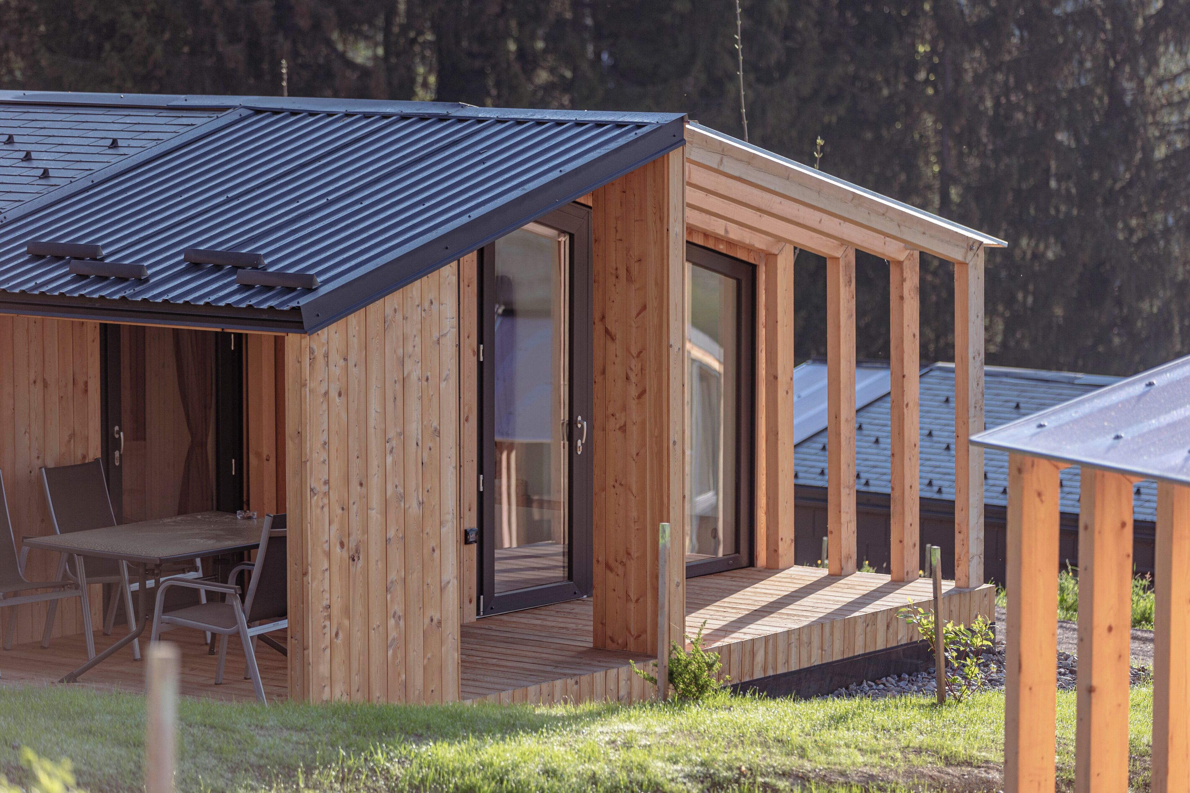 A wooden cabin with a sloped roof, large glass doors, and a patio area with outdoor furniture.