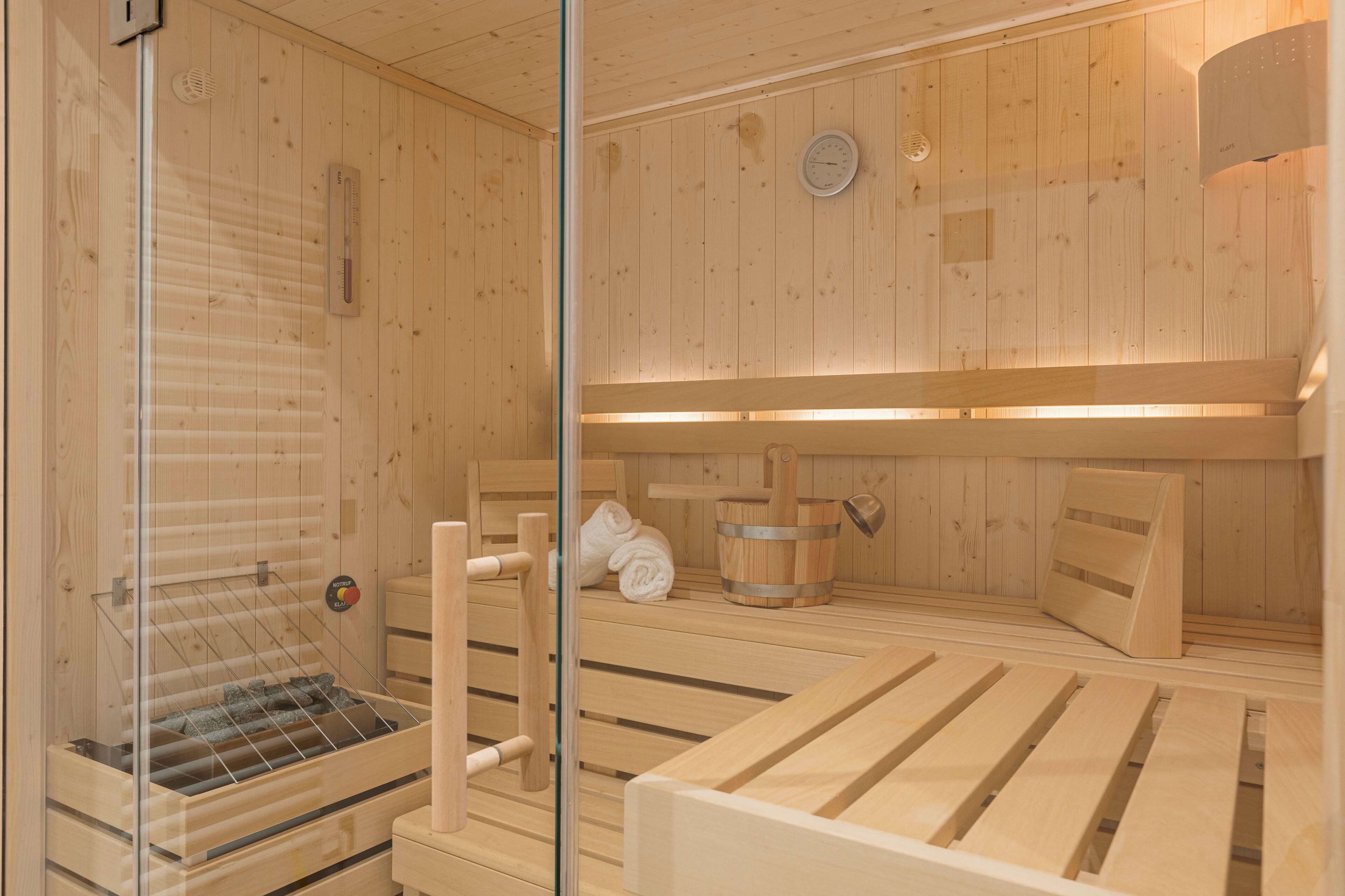 A wooden sauna with benches, a glass door, and a towel rack.