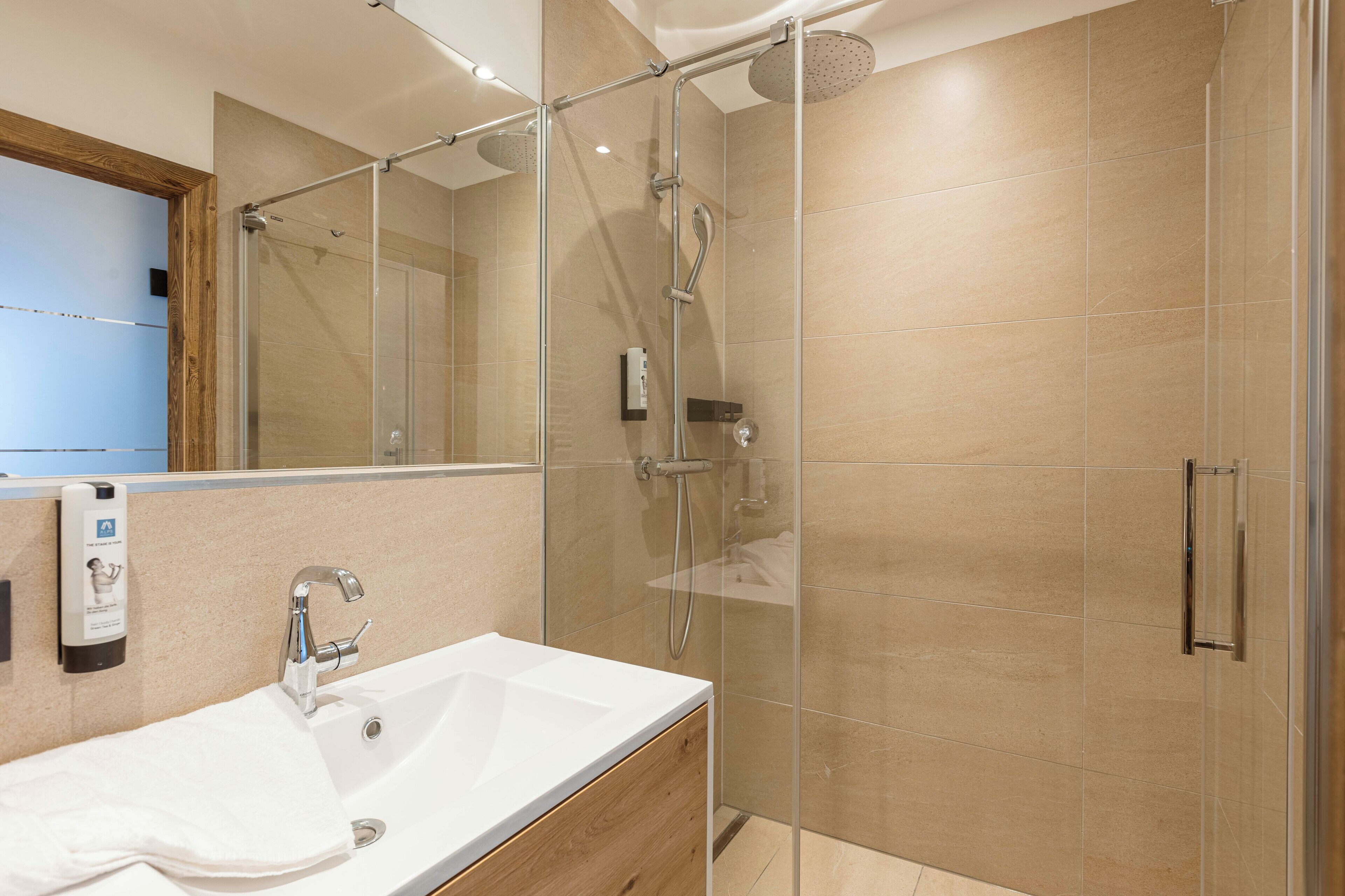 Een moderne badkamer met een douchecabine van glas, een houten wastafelmeubel met een witte wasbak en een grote spiegel.