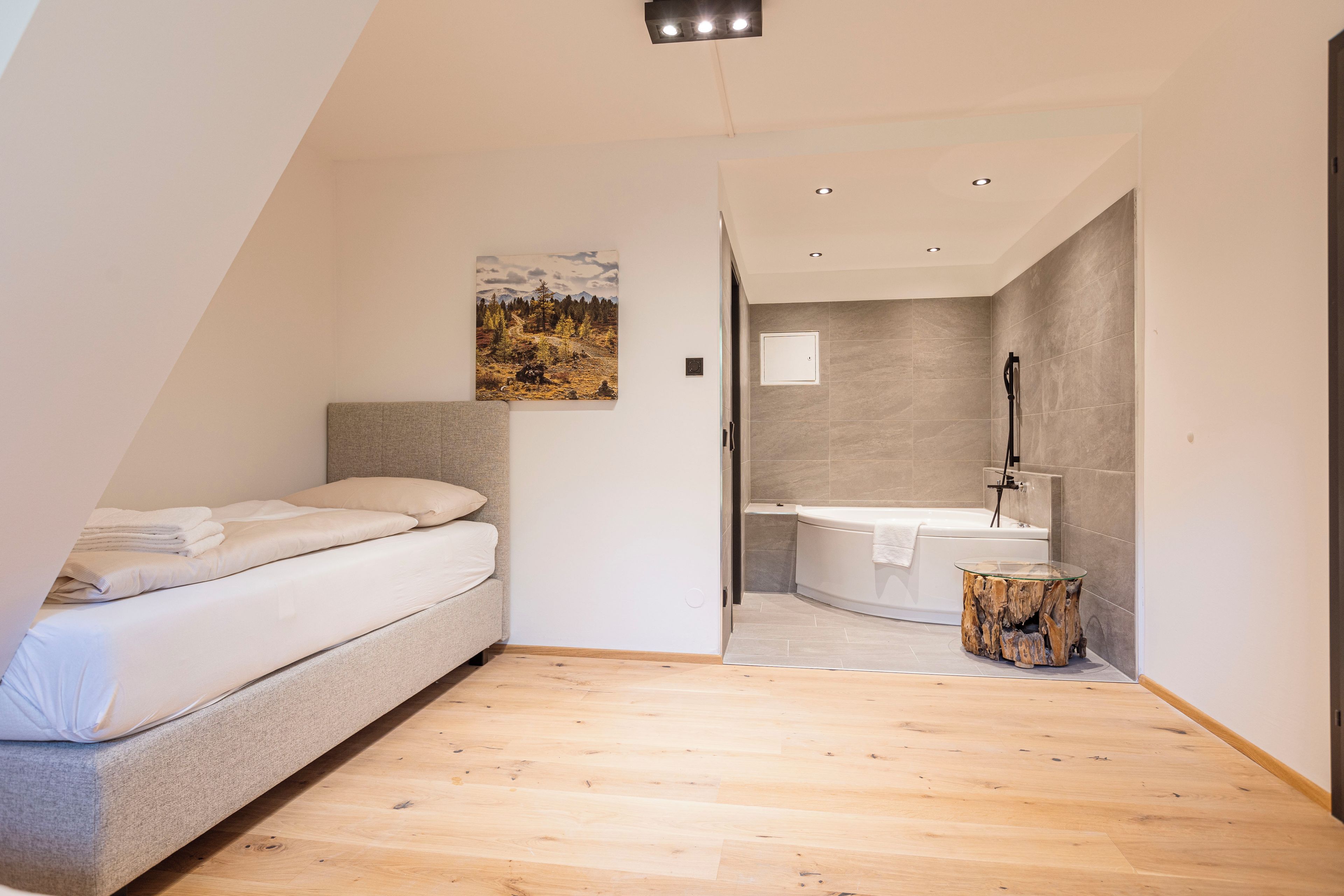 A modern bedroom with a bed, a painting, and a bathroom with a bathtub and sink.