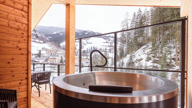 Un baño moderno con una bañera grande, una cubierta de madera y una vista panorámica de un pueblo nevado.