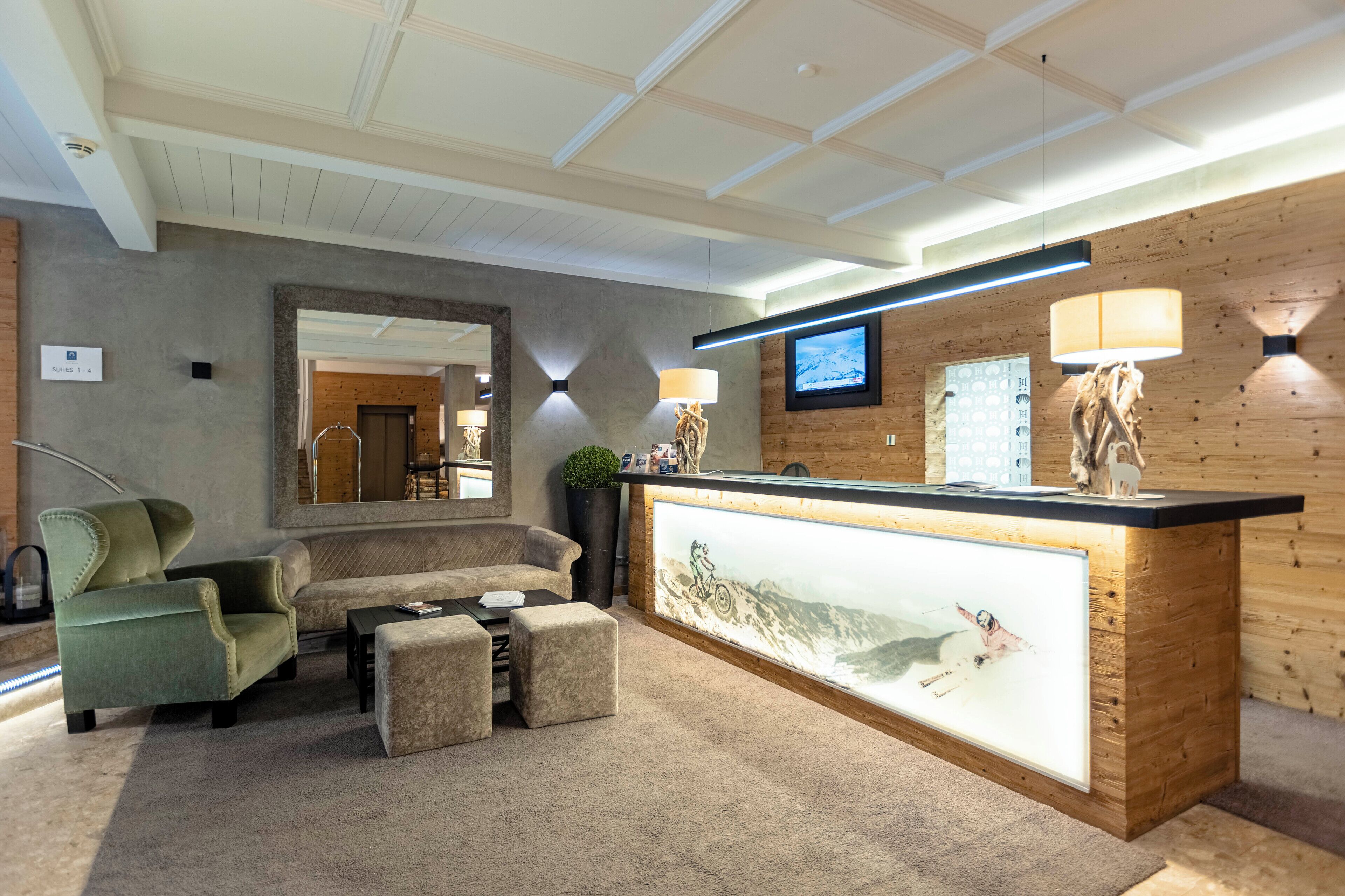 A reception area with a wooden reception desk, a large mirror, and a seating area with a green armchair and ottomans.