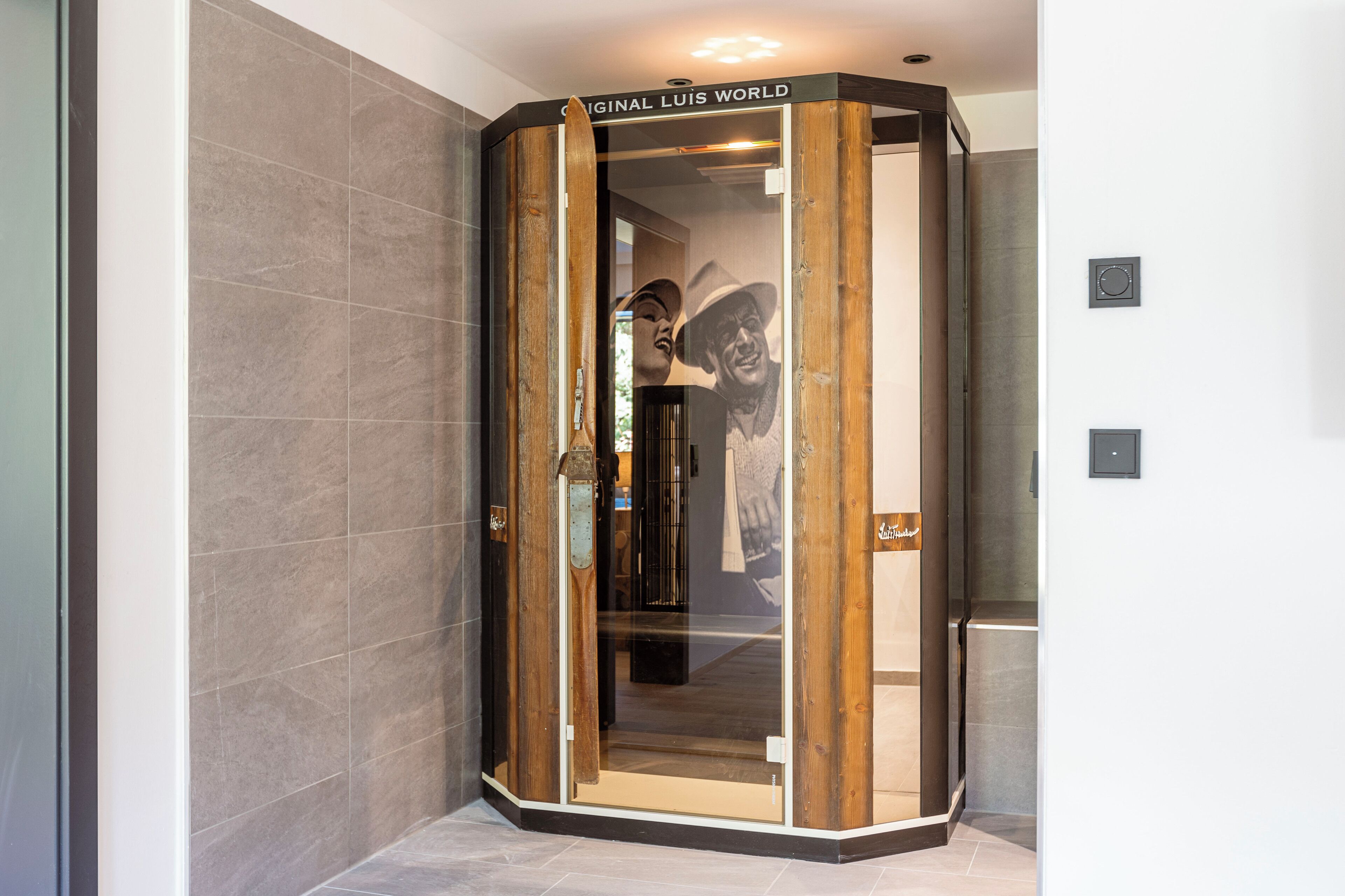 A corner elevator with a glass door and a wooden frame, featuring a sign that reads "Original Luis World".
