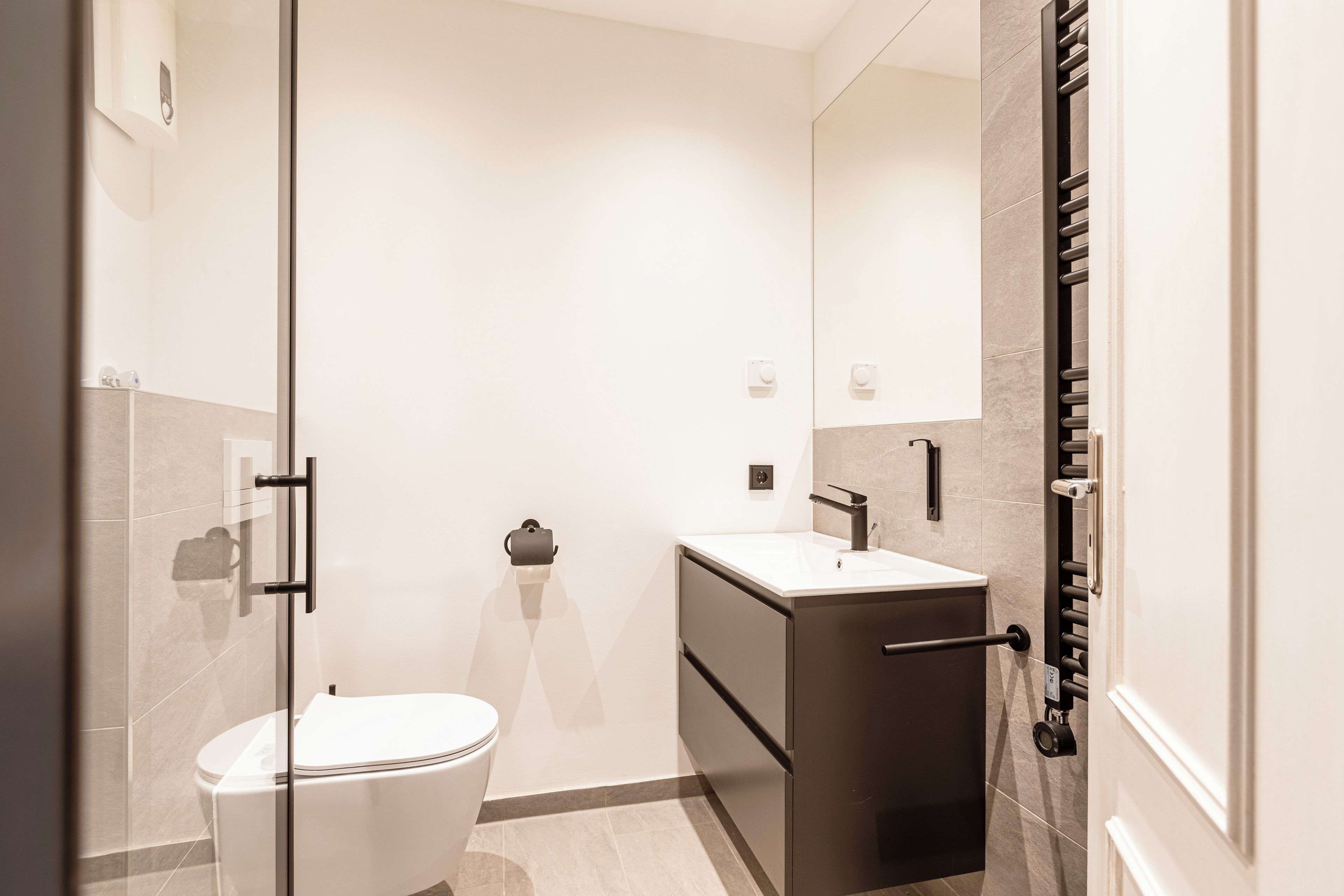 A modern bathroom with a glass shower enclosure, a white toilet, a dark vanity with a sink, and a towel rack.