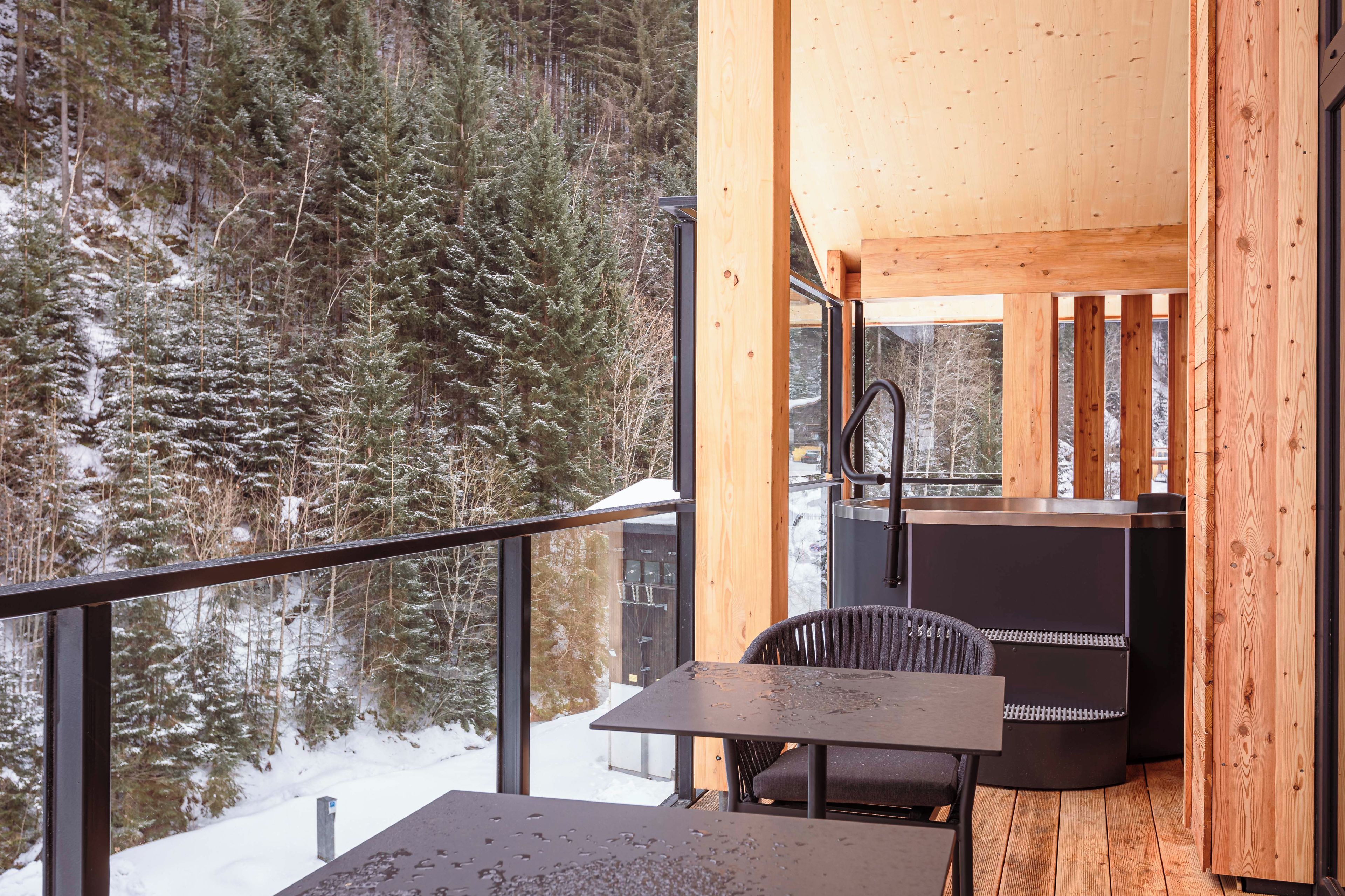 A wooden cabin with a balcony, a table, and a chair.