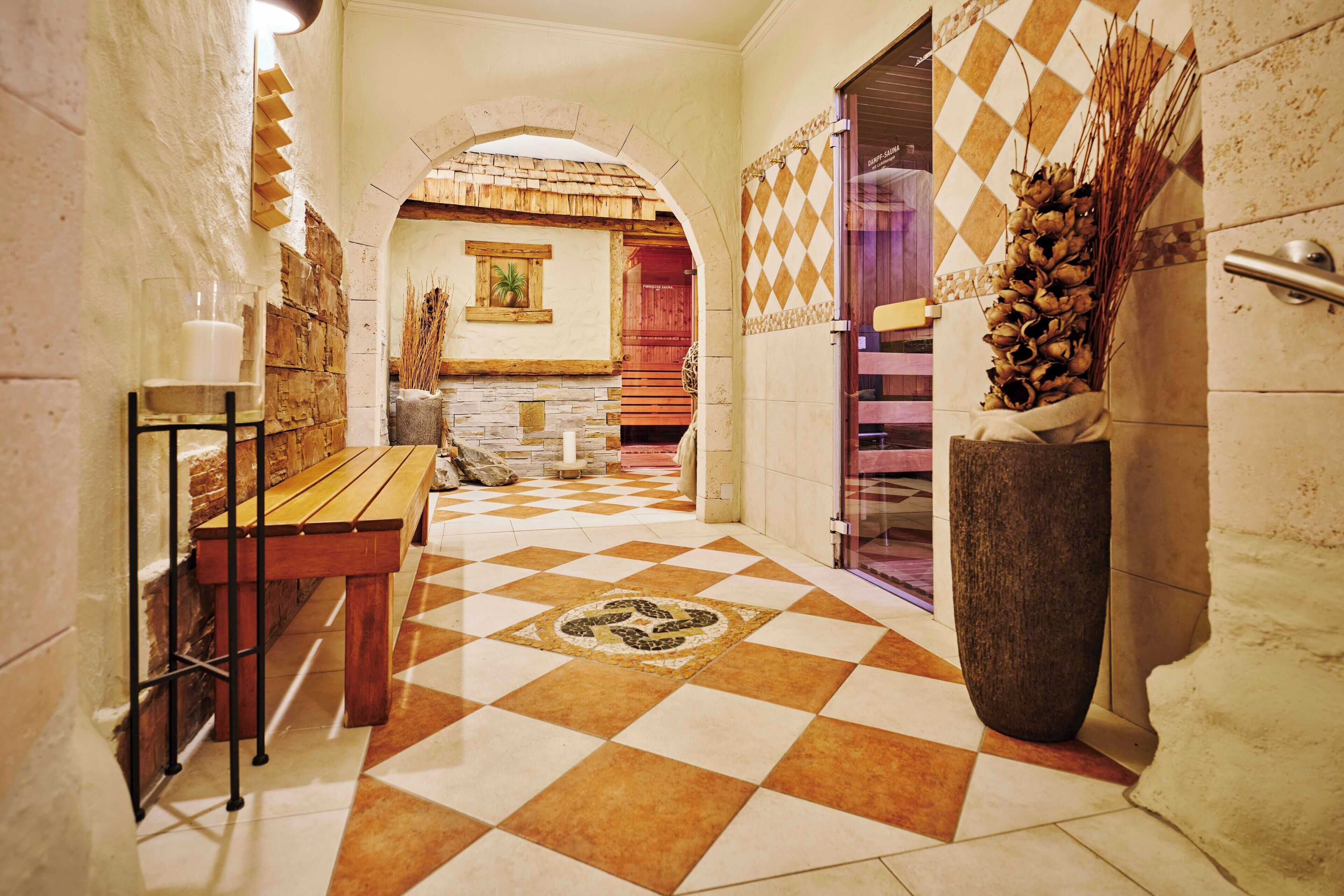 A checkered floor, a wooden bench, a stone wall, and a large vase with dried plants.