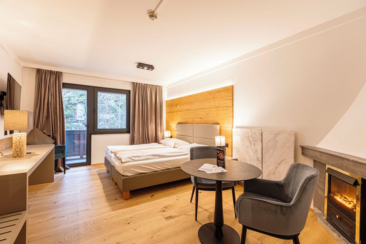 Ein modernes Hotelzimmer mit einem Bett, einem Schreibtisch, einem Sessel, einem runden Tisch und einem Kamin.