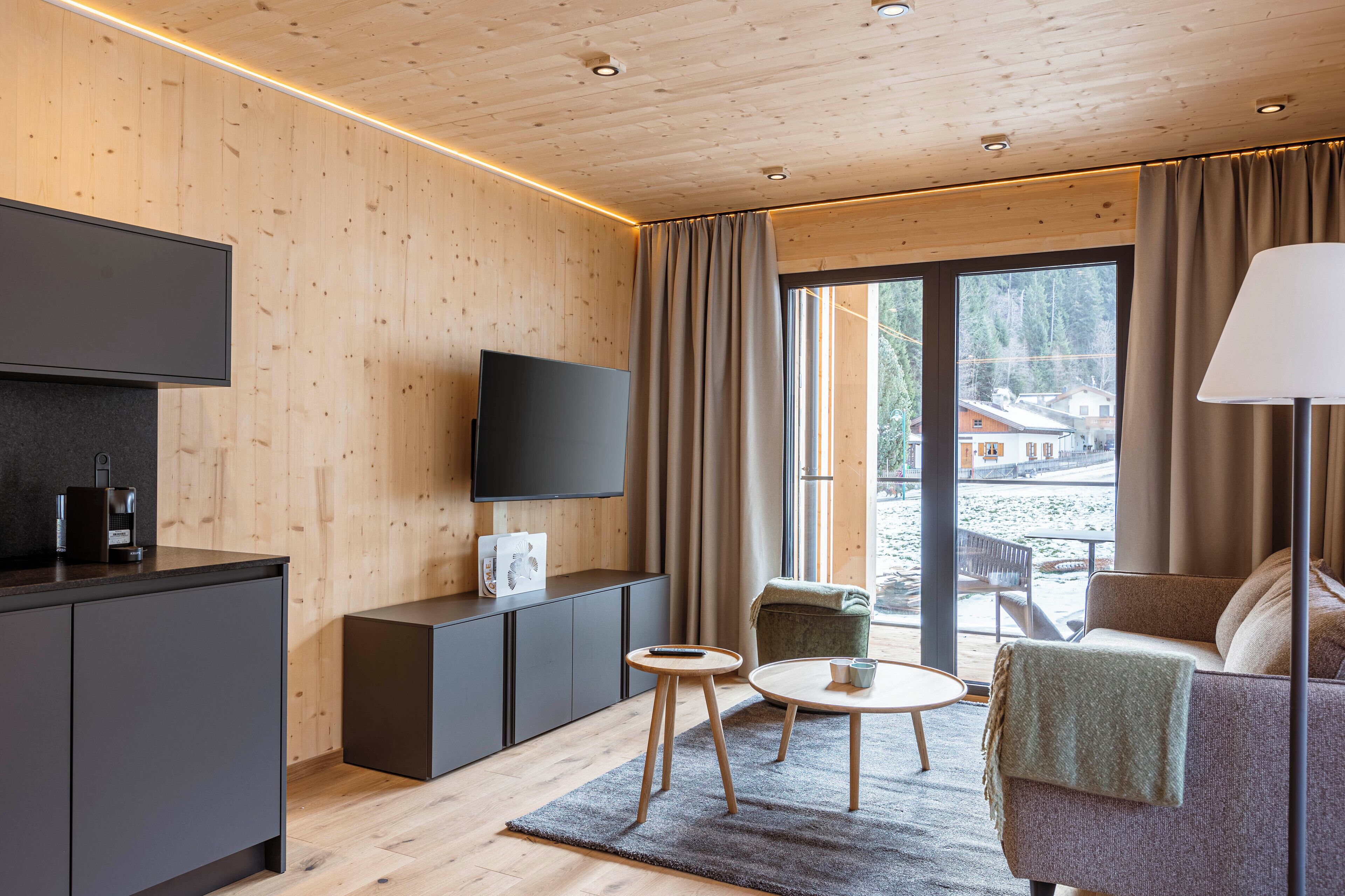 Ein modernes Wohnzimmer mit Flachbildfernseher, einer Couch, einem Couchtisch und einem Essbereich mit Tisch und Stühlen.
