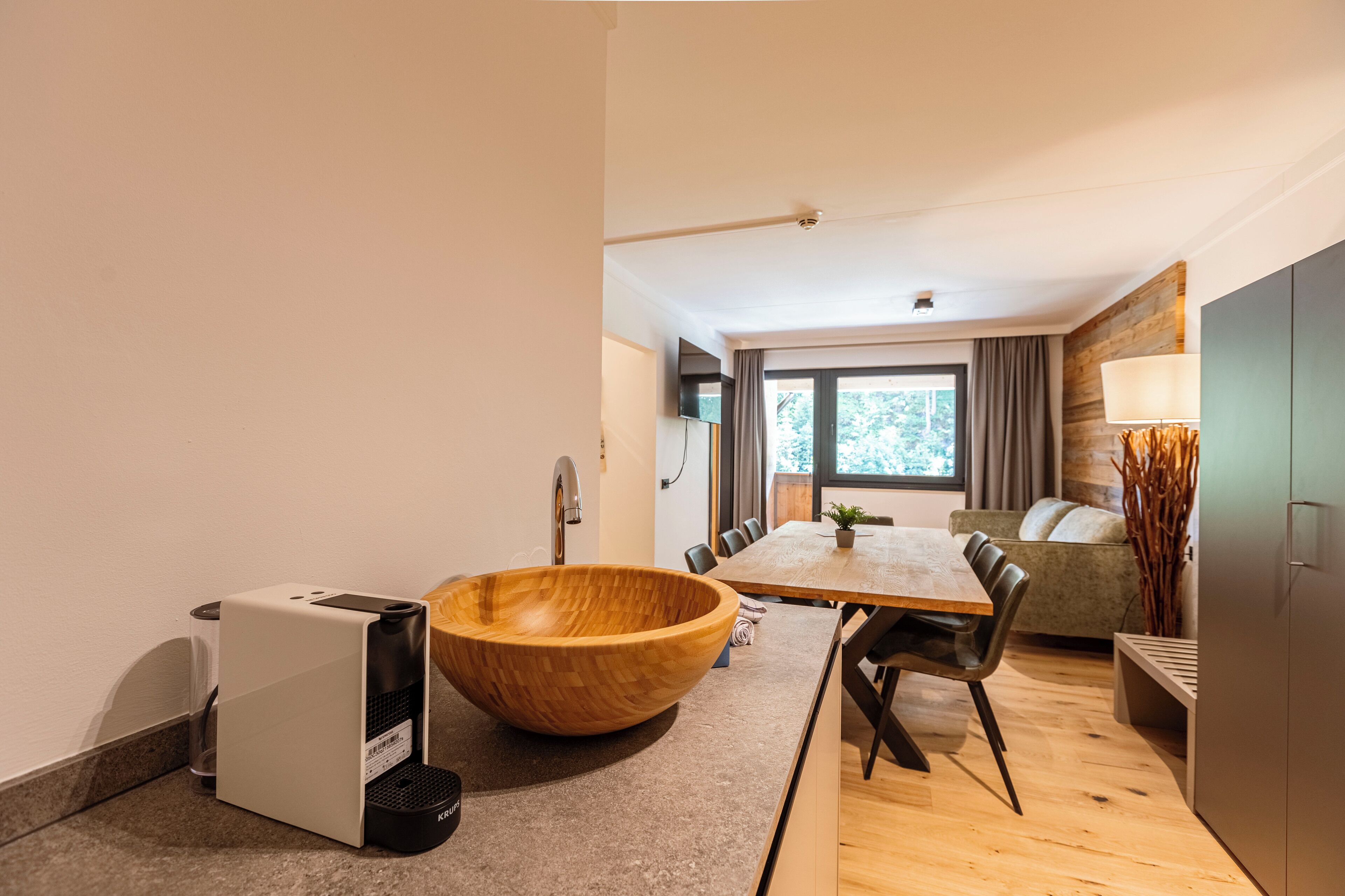 A modern kitchen with a wooden bowl sink, a coffee machine, and a dining area with a wooden table and chairs.