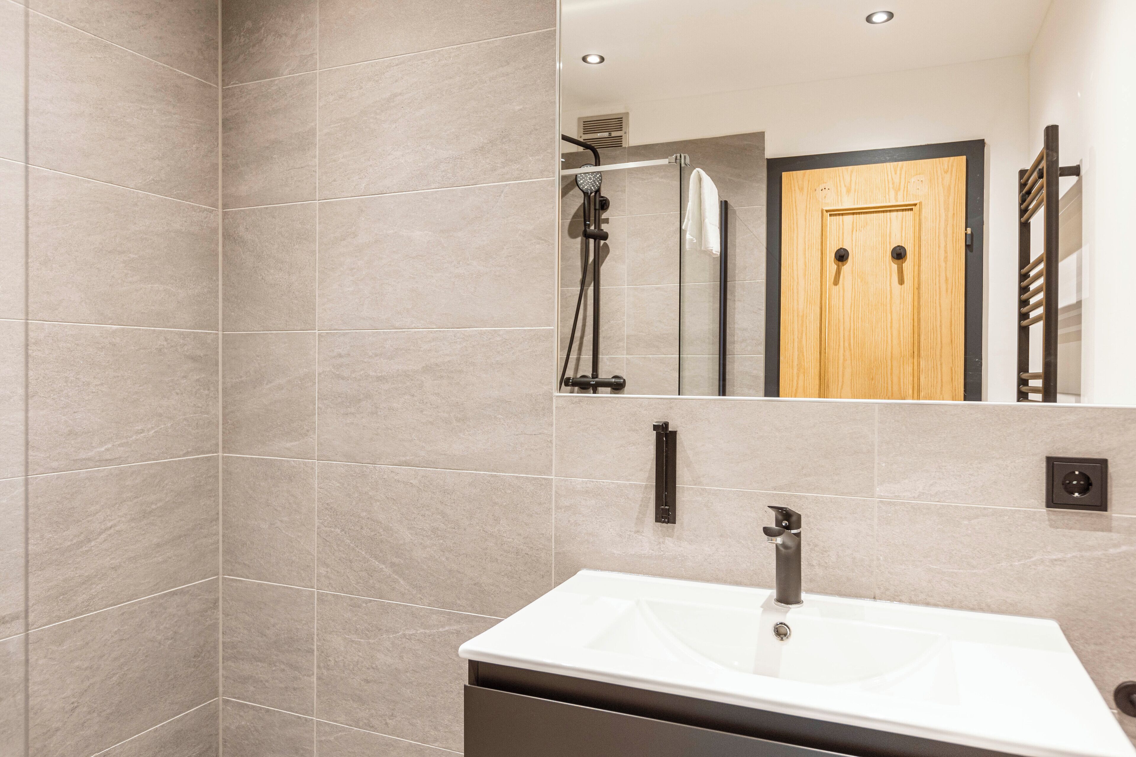 Un baño moderno con un espejo grande, un lavabo y zona de ducha.