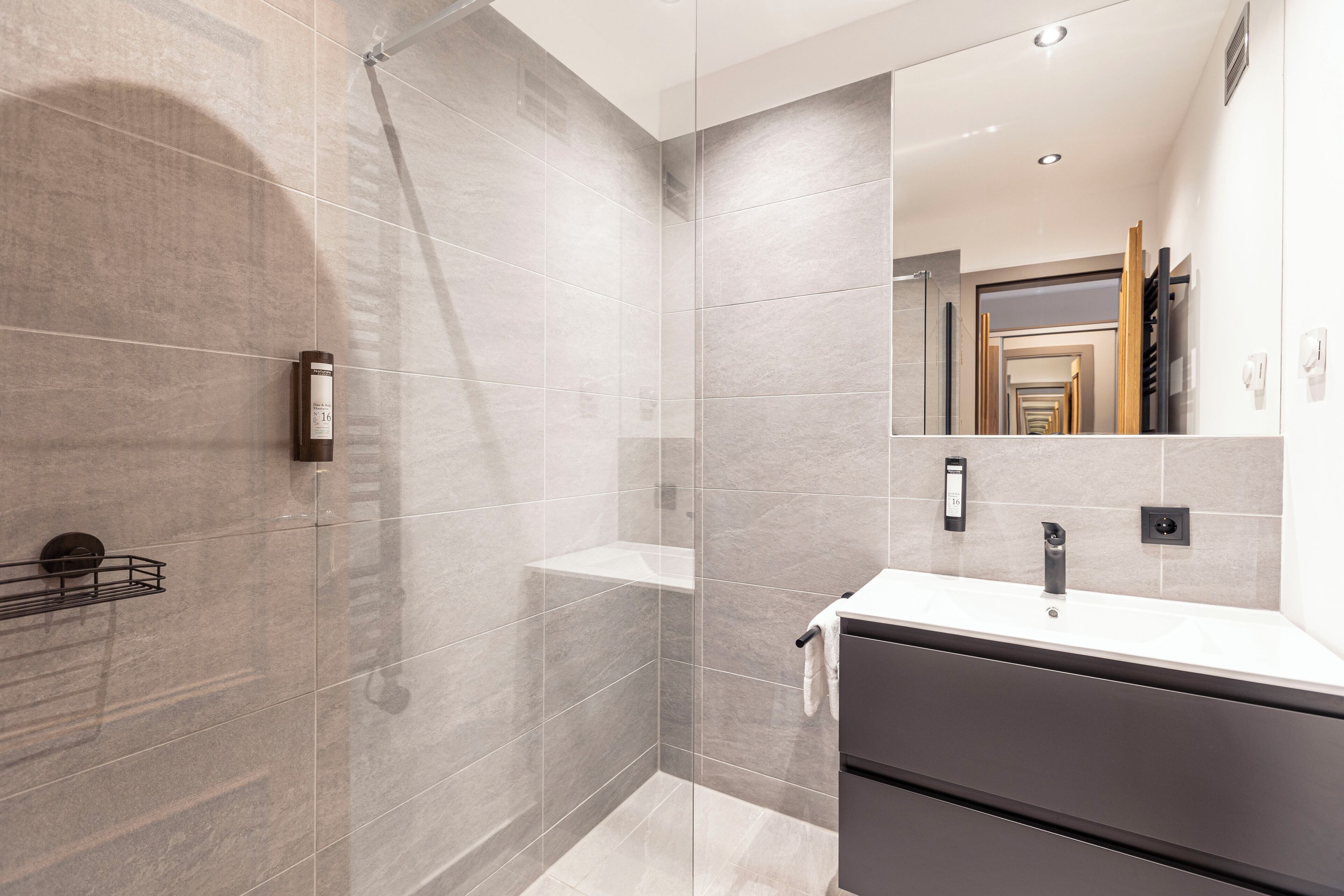Un baño moderno con ducha de vidrio, tocador con espejo y perchero para toallas.