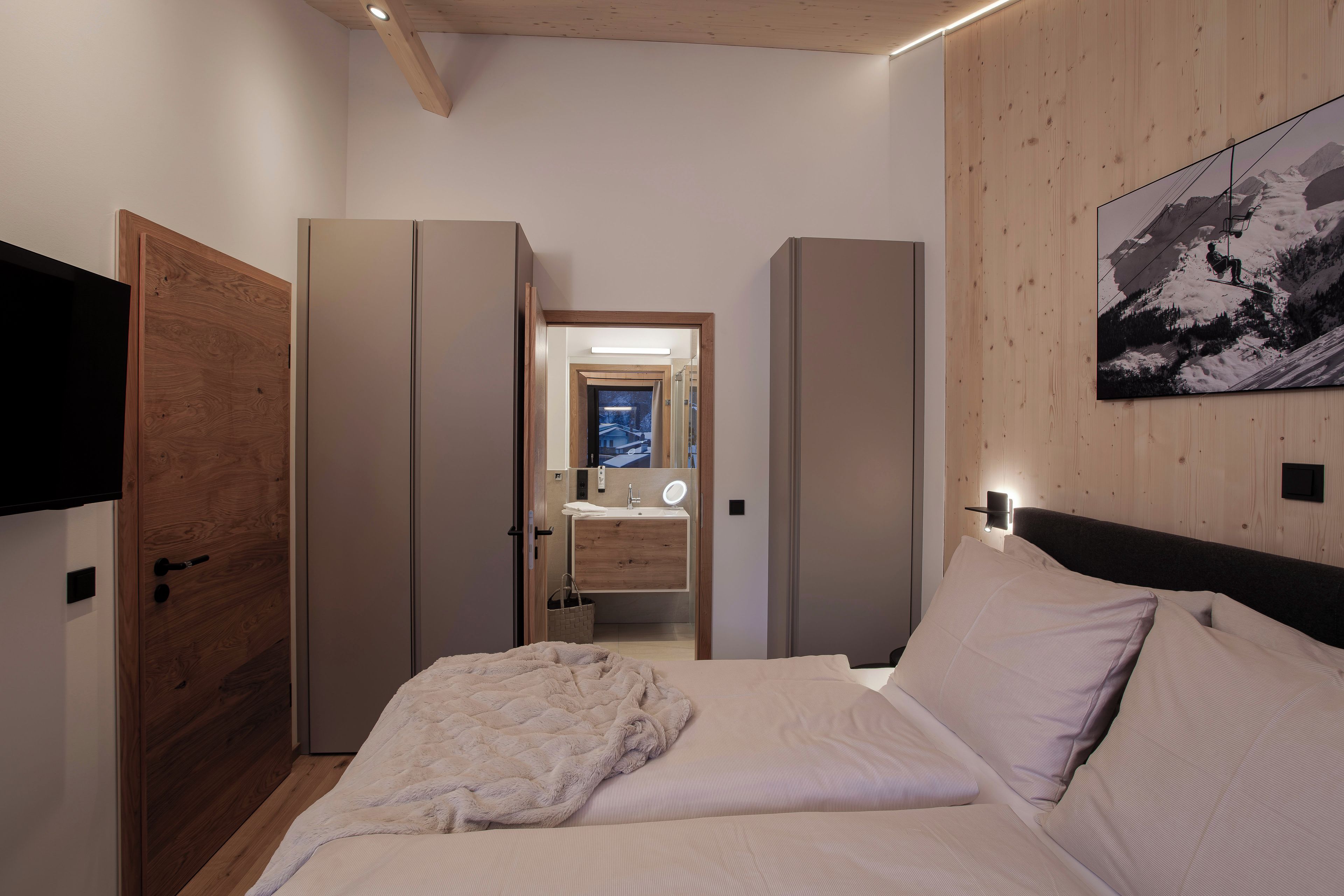 A bedroom with a bed, a wooden wardrobe, a mirror, and a painting on the wall.