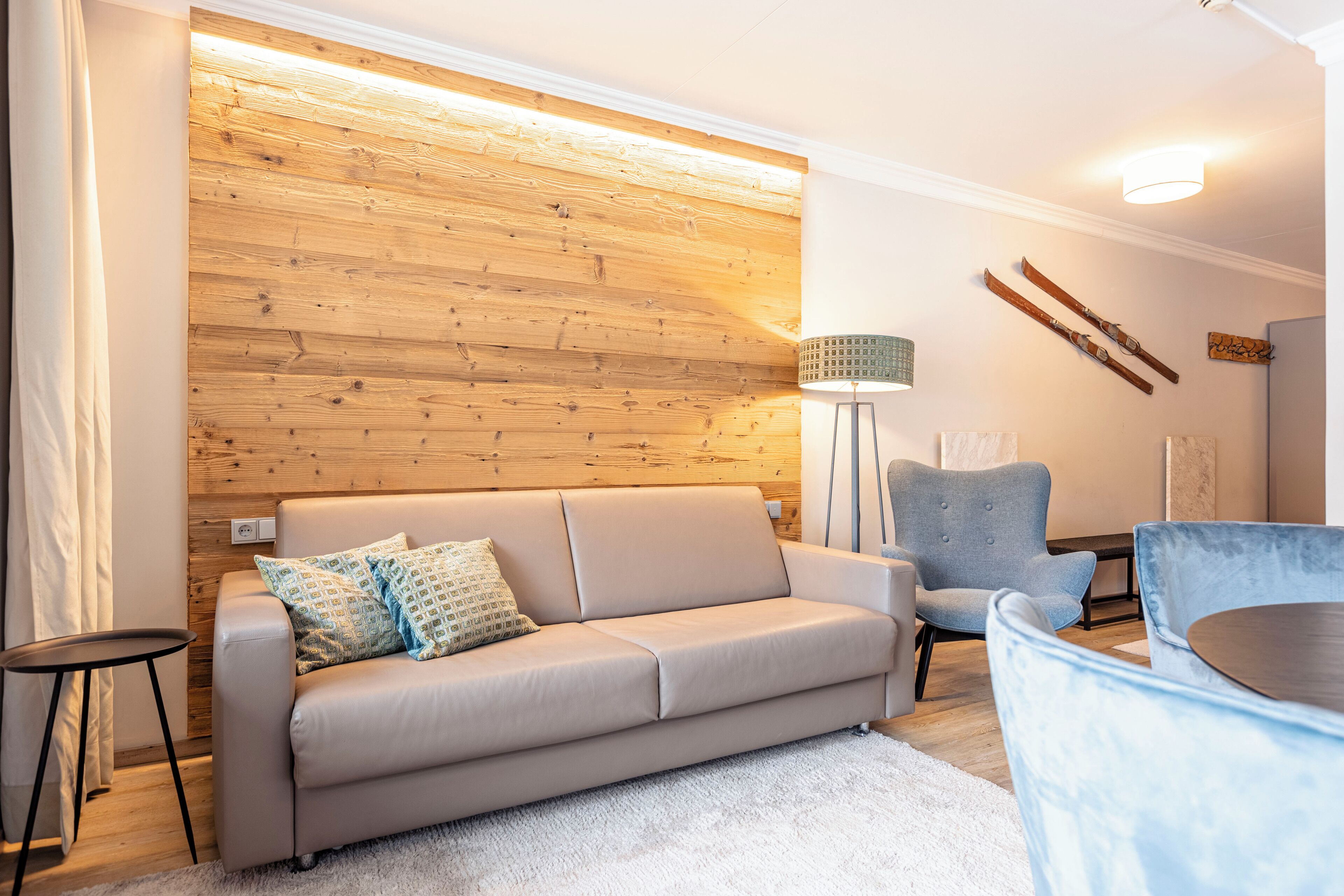 A modern living room with a wooden accent wall, a beige sofa, a blue armchair, and a small round table.