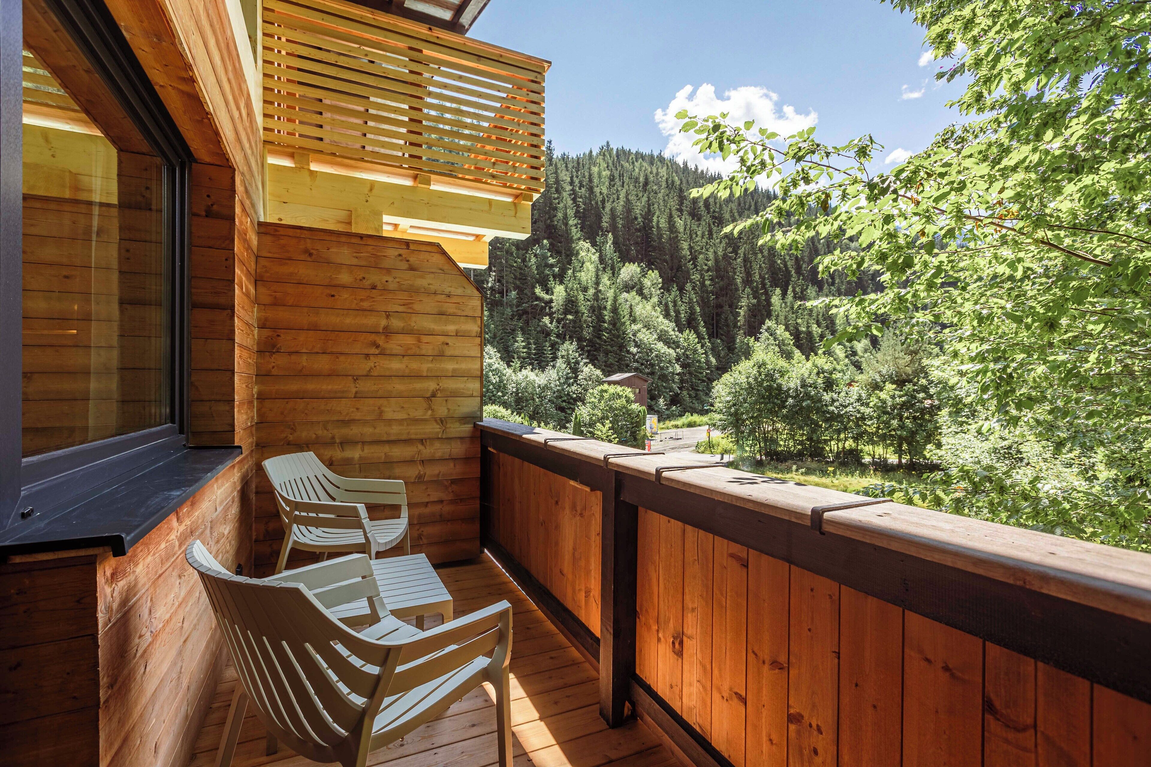 A wooden deck with two chairs and a table, overlooking a forested valley.