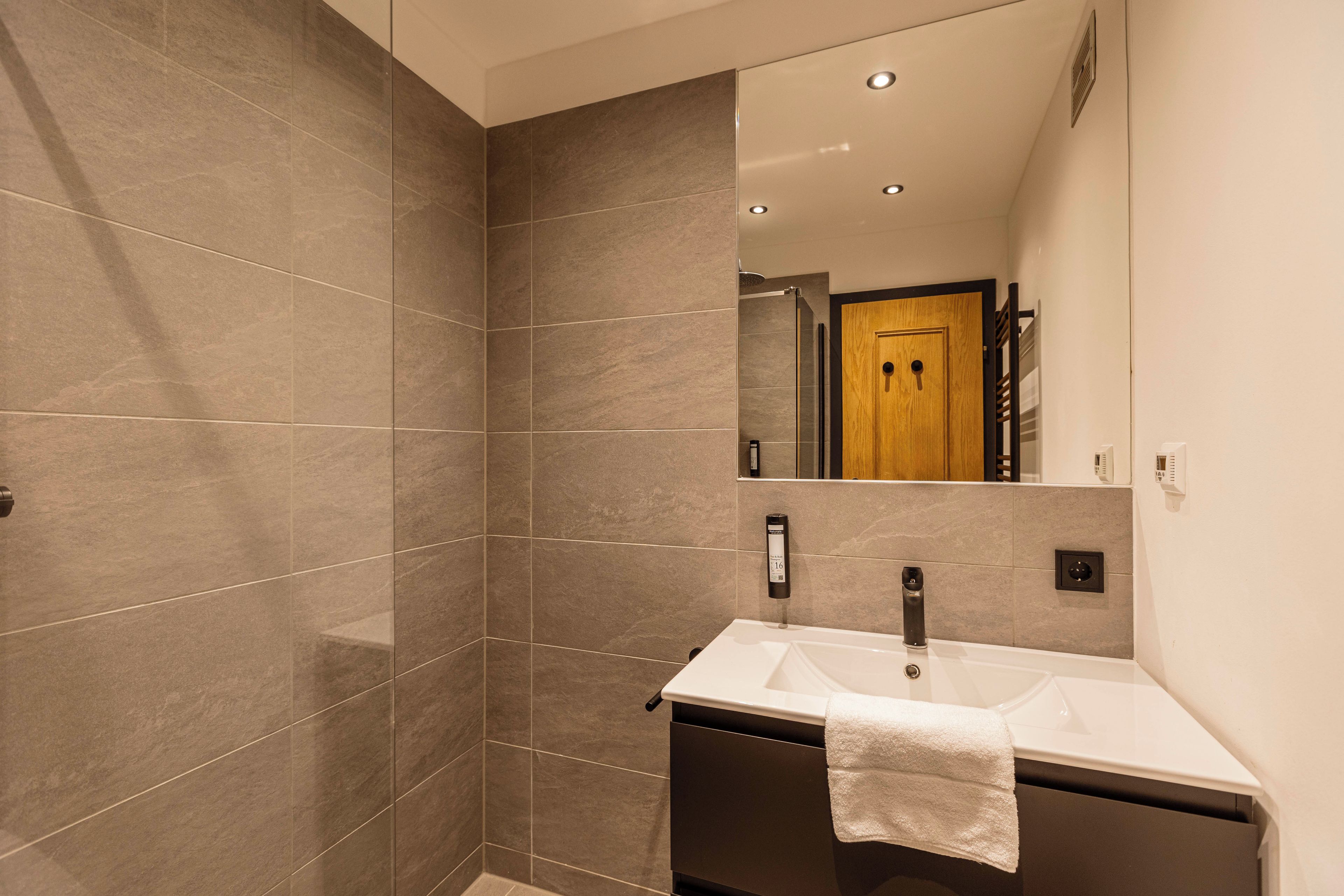 A modern bathroom with a large mirror, a white sink, and a towel hanging on the wall.