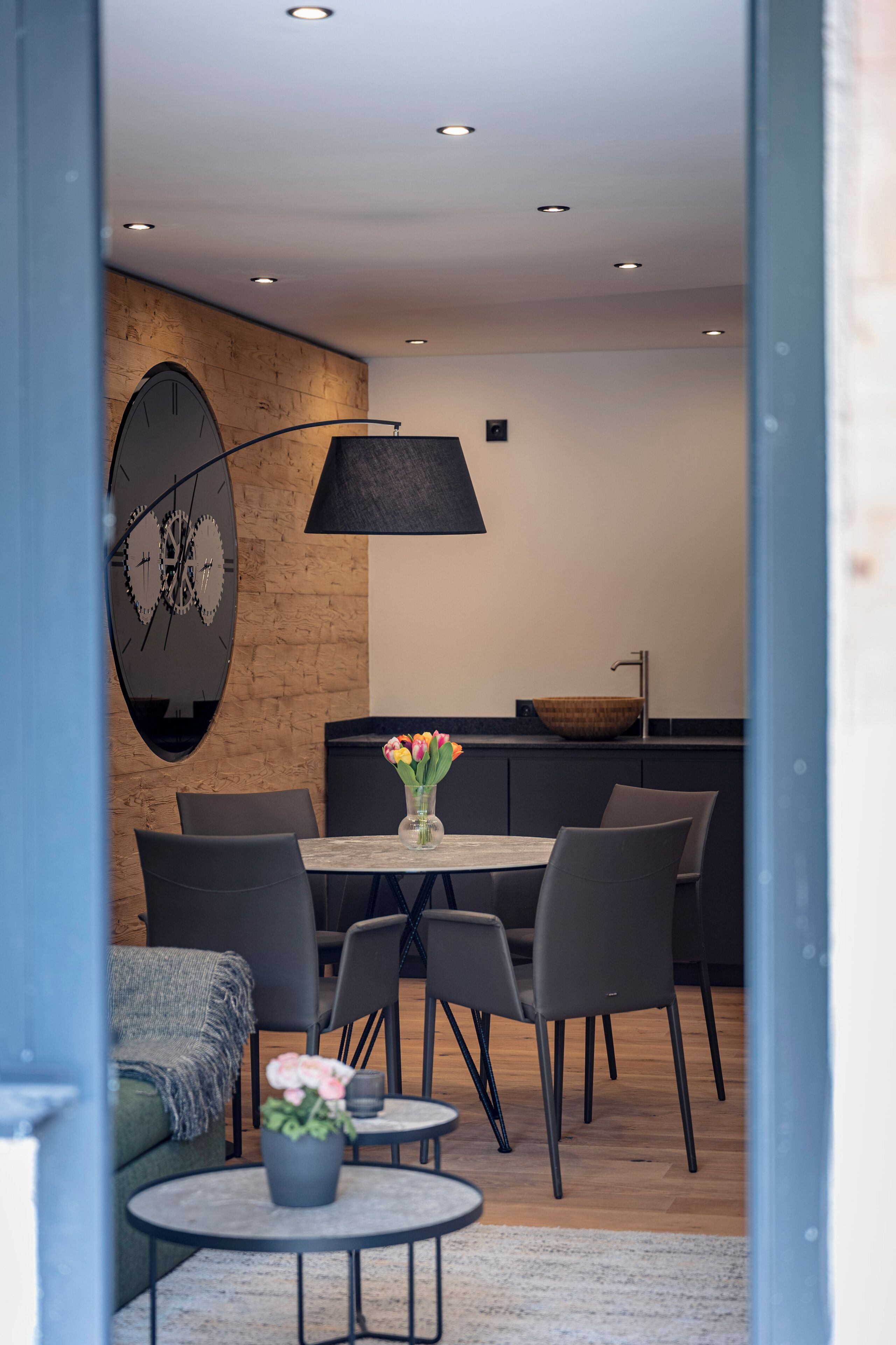 Un comedor moderno con una pared de madera, un reloj grande y un lavamanos en forma de cuenco.