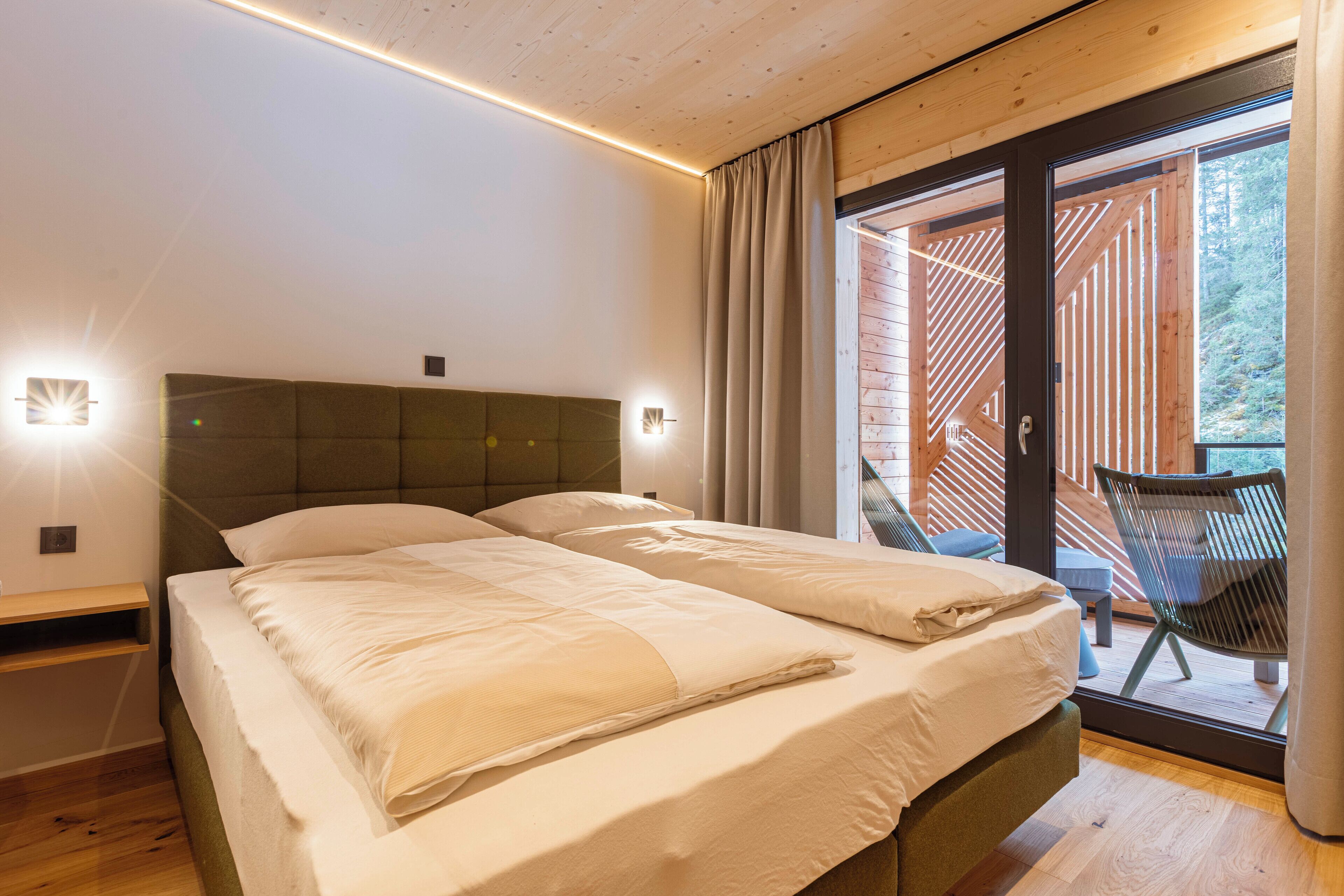 Un dormitorio con dos camas, techo de madera, puerta de vidrio corredera a un balcón y una silla afuera.