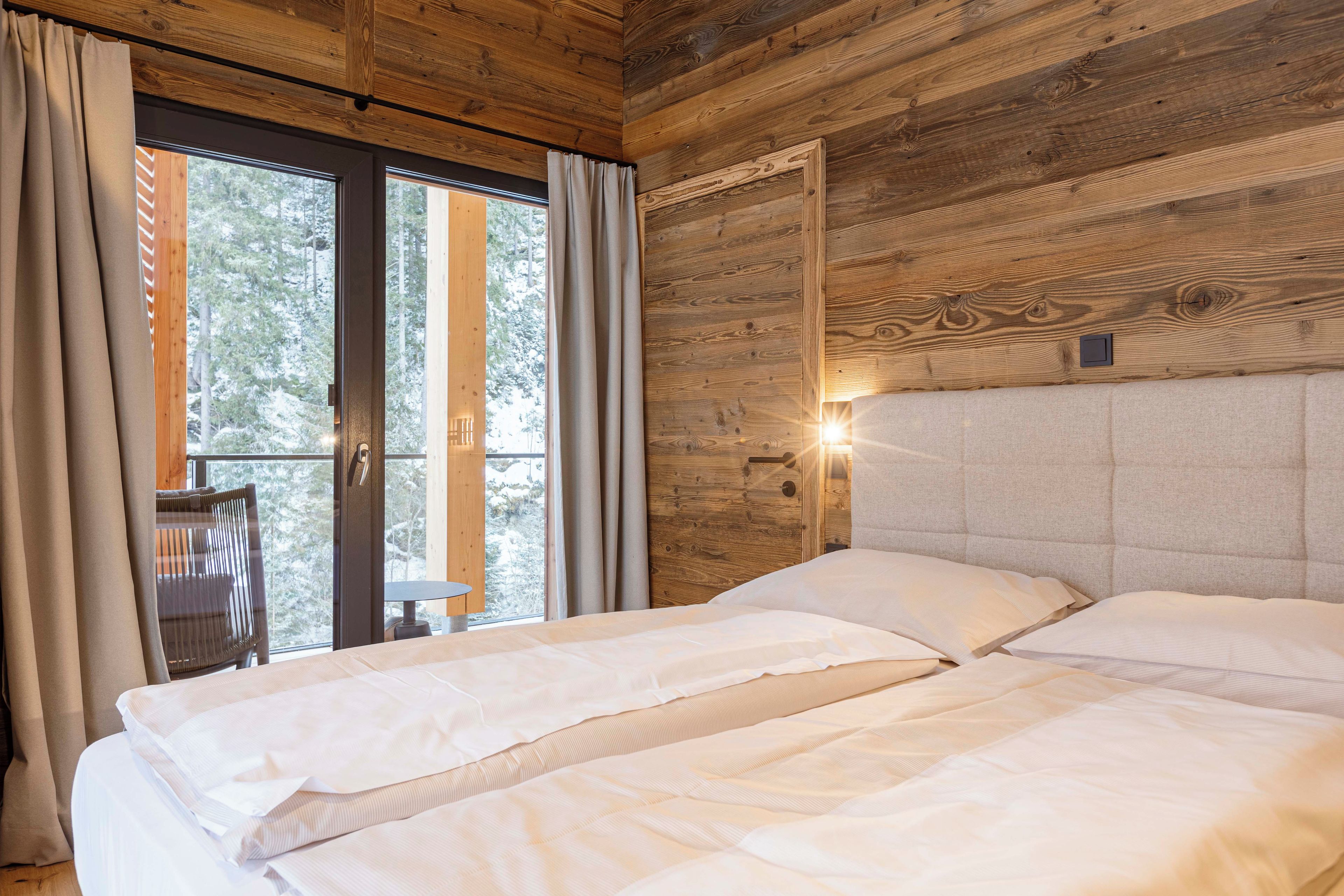 A wooden cabin room with a bed, curtains, and a window.
