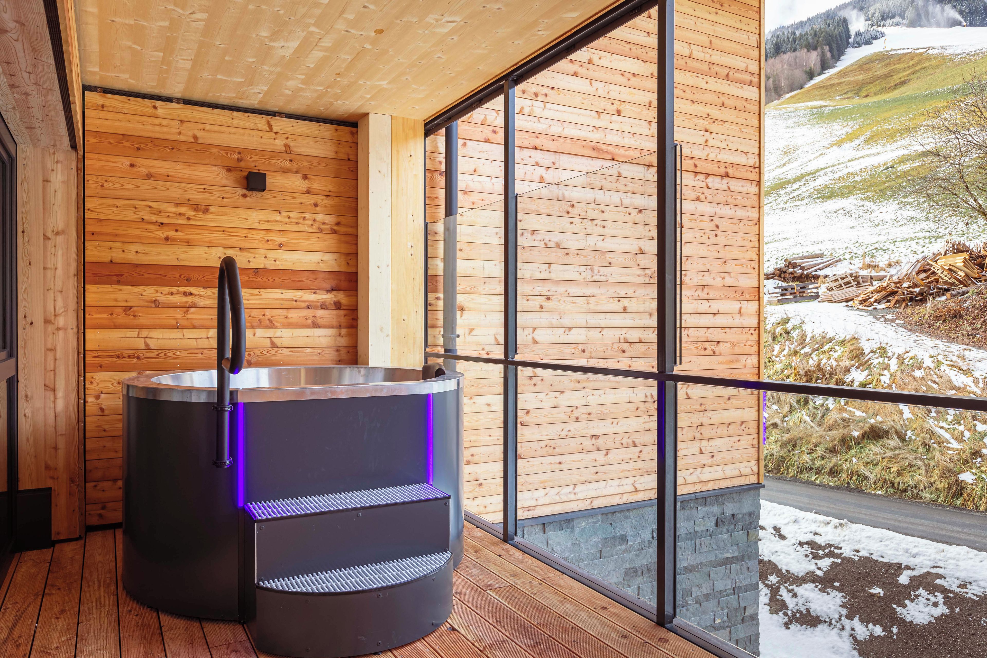A sauna with a wooden interior and a view of a snowy landscape through large windows.