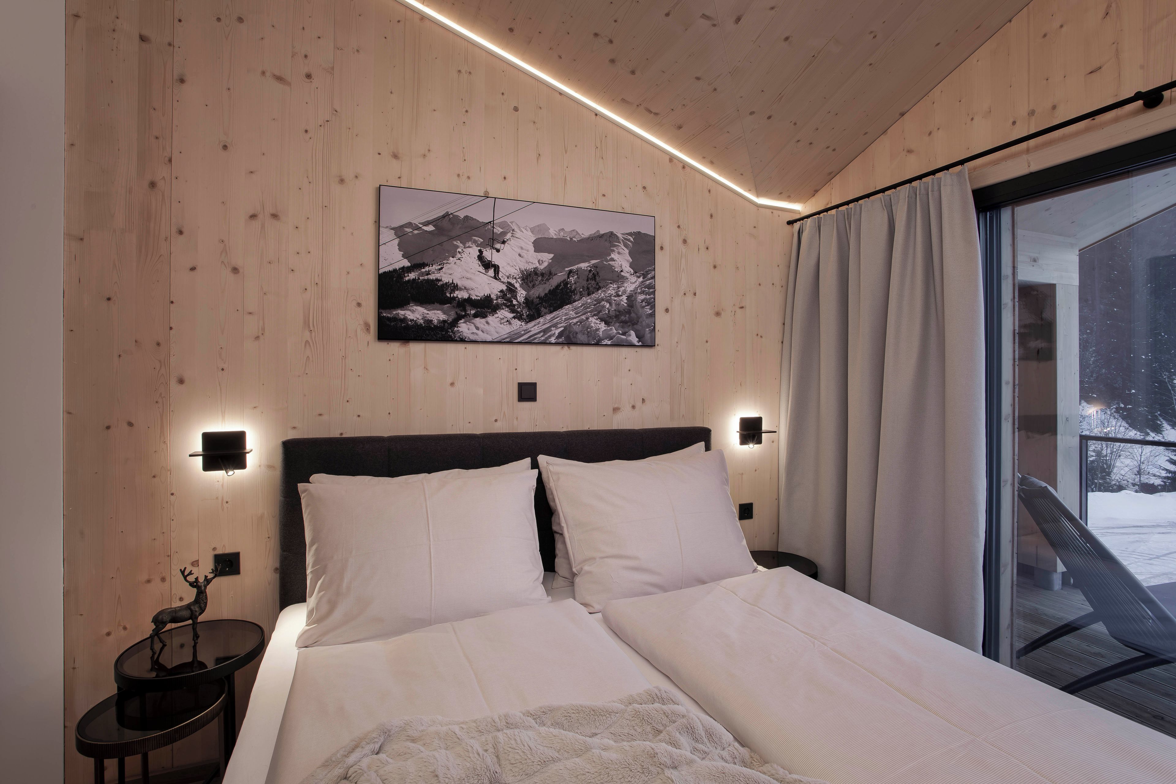 Une chambre moderne avec un plafond en bois, un grand lit avec une literie blanche, un tableau représentant un paysage de montagne et une fenêtre avec des rideaux.