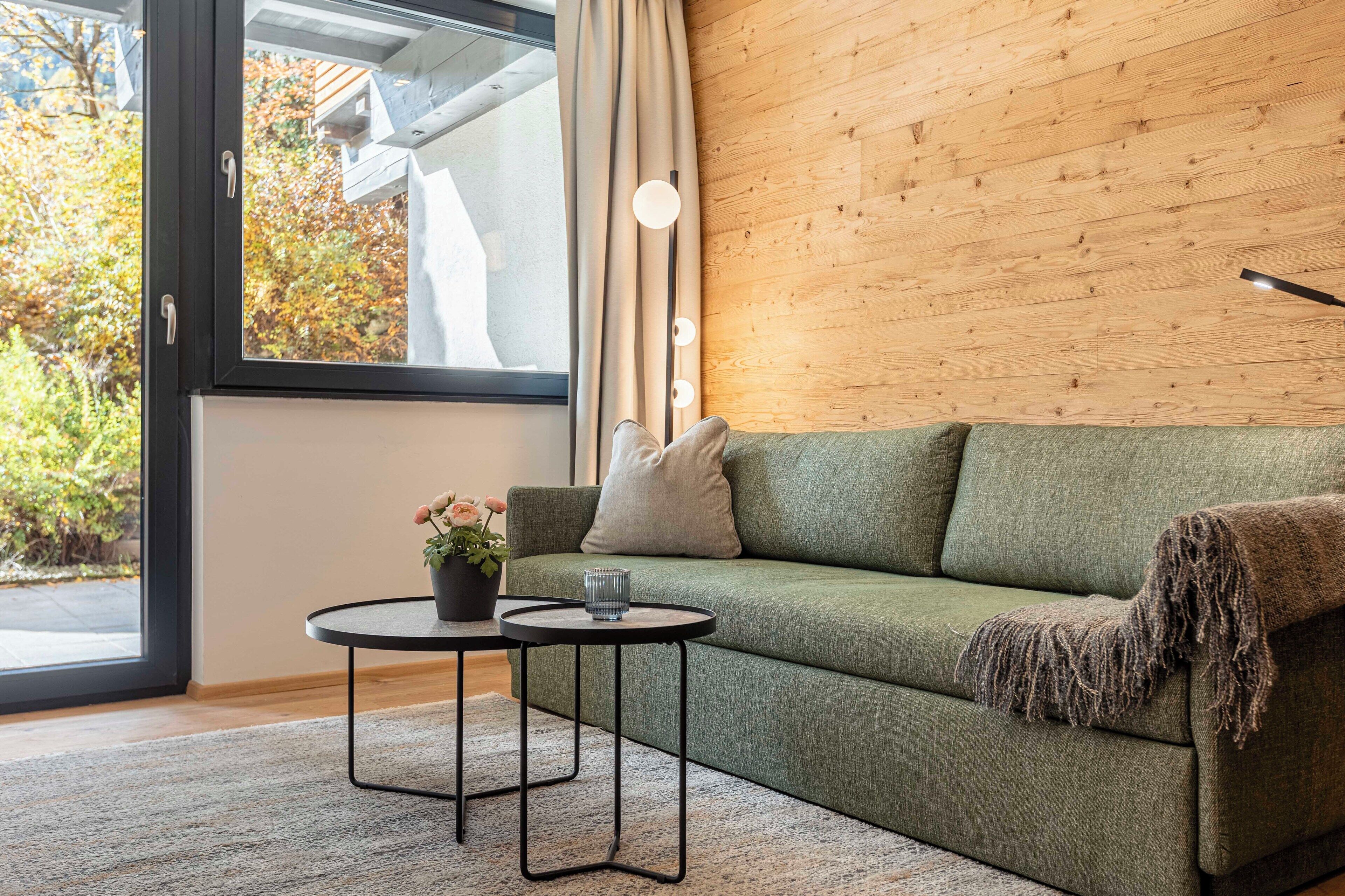 Een moderne woonkamer met een groene bank, een klein rond tafeltje en een potplant.